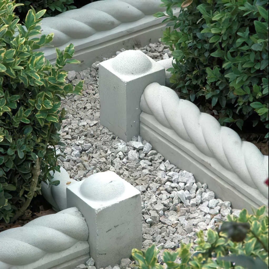 Weiße steinerne Gartenumrandung mit Kiesbett und grünem Pflanzenbesatz