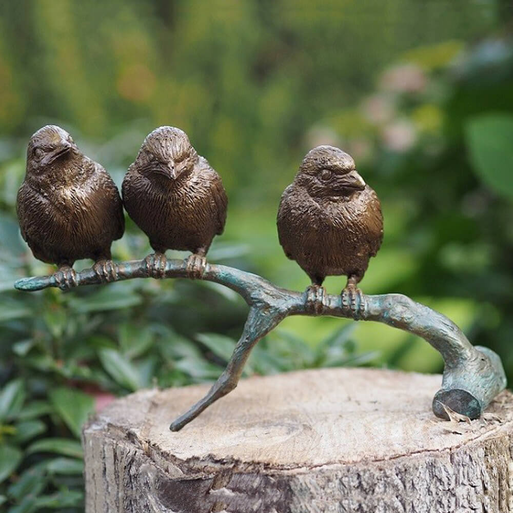 Tre statuette di uccelli color bronzo su un ramo posizionate su un ceppo in giardino