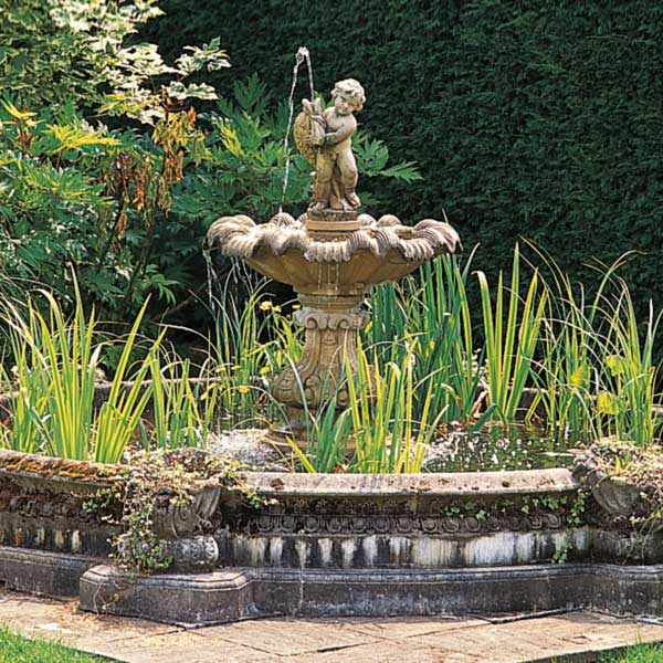 Steinbrunnen im Garten mit Engel-Figur und umgeben von Pflanzen