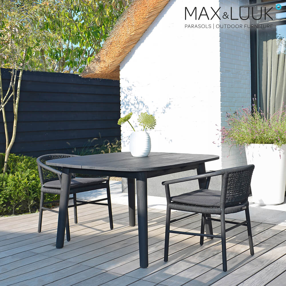 Table de jardin noire avec deux chaises sur terrasse en bois devant une maison blanche et un jardin
