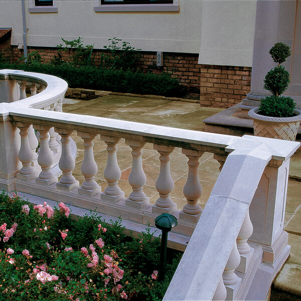 Weißes steinernes Geländer an einer Gartenterrasse mit Blumenbeet im Vordergrund
