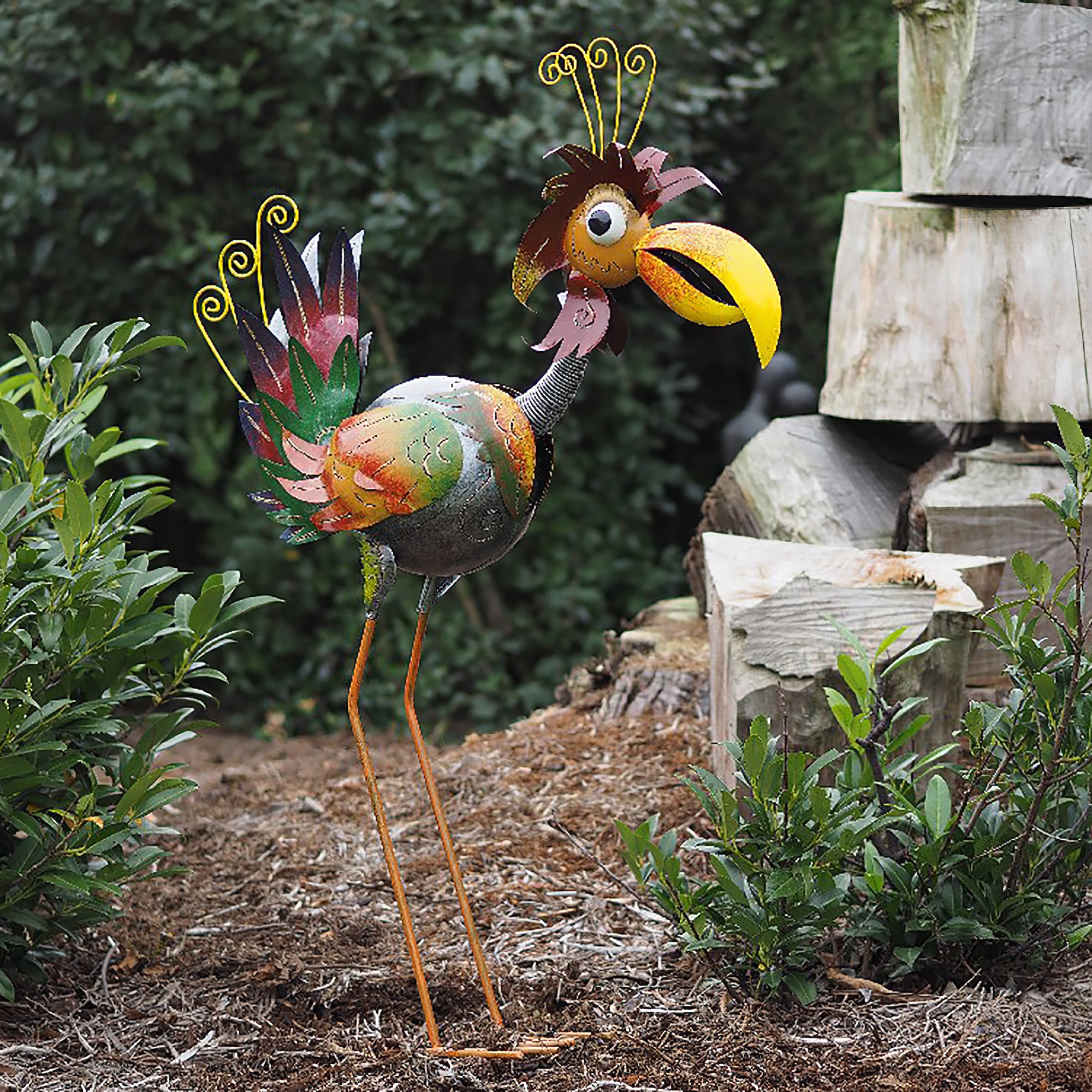 Bunte Metall-Gartenfigur eines Vogels in einem Garten neben Steinen und Pflanzen