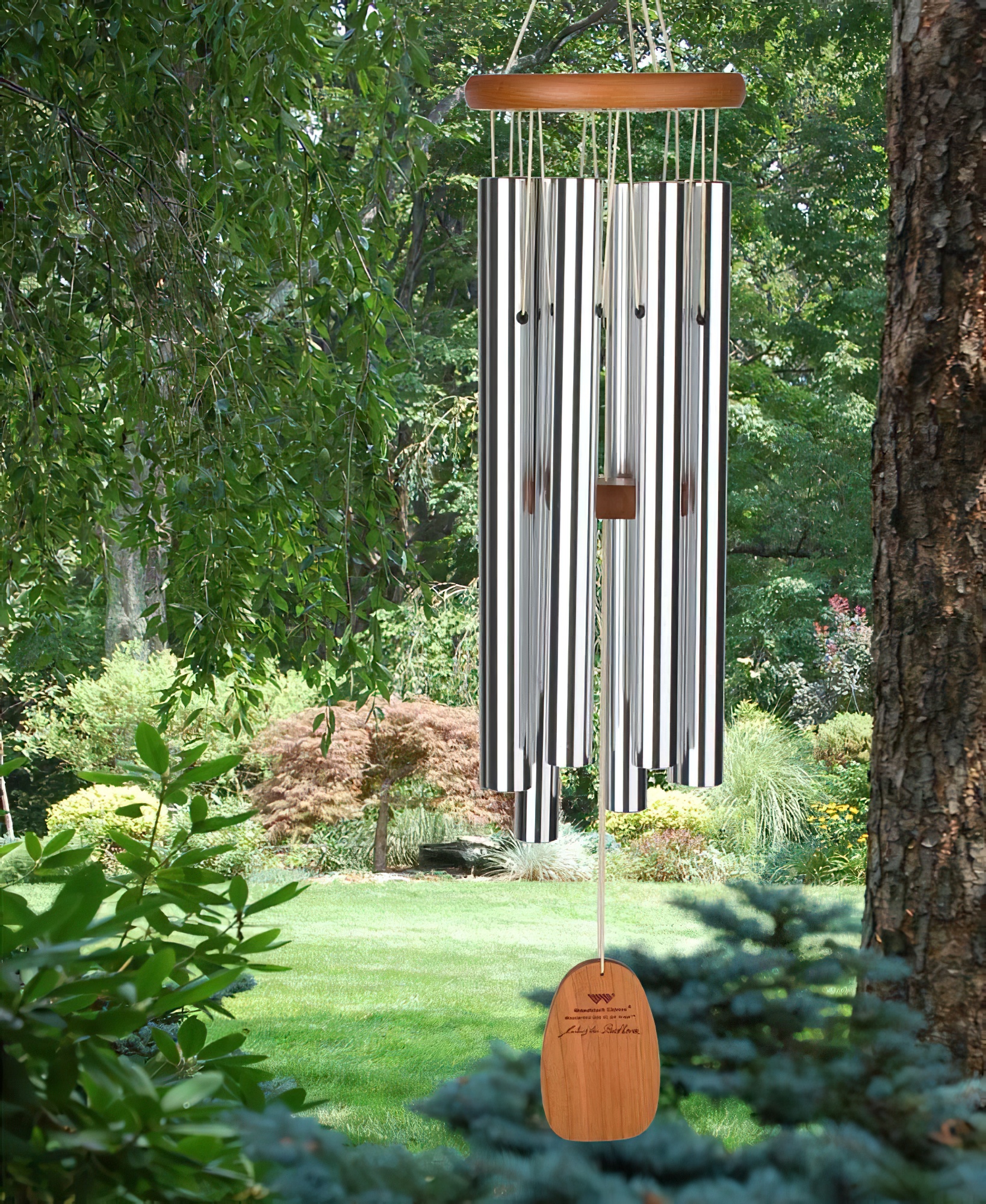 Carillon en bois et métal suspendu dans un jardin verdoyant entre des arbres