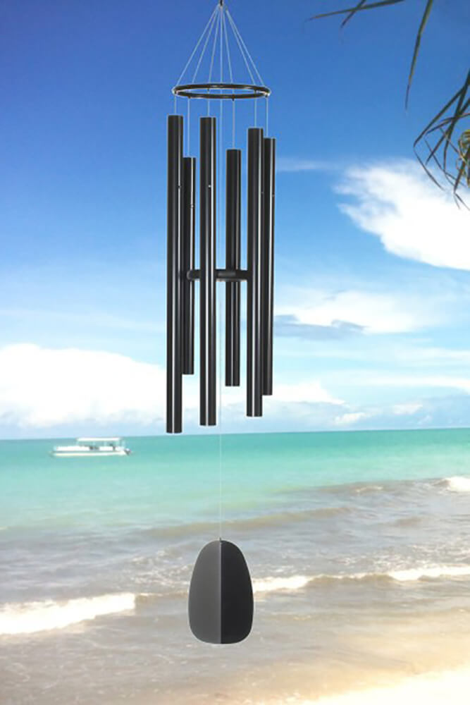 Campane a vento nere appese sotto un cielo blu sopra una spiaggia sabbiosa e il mare