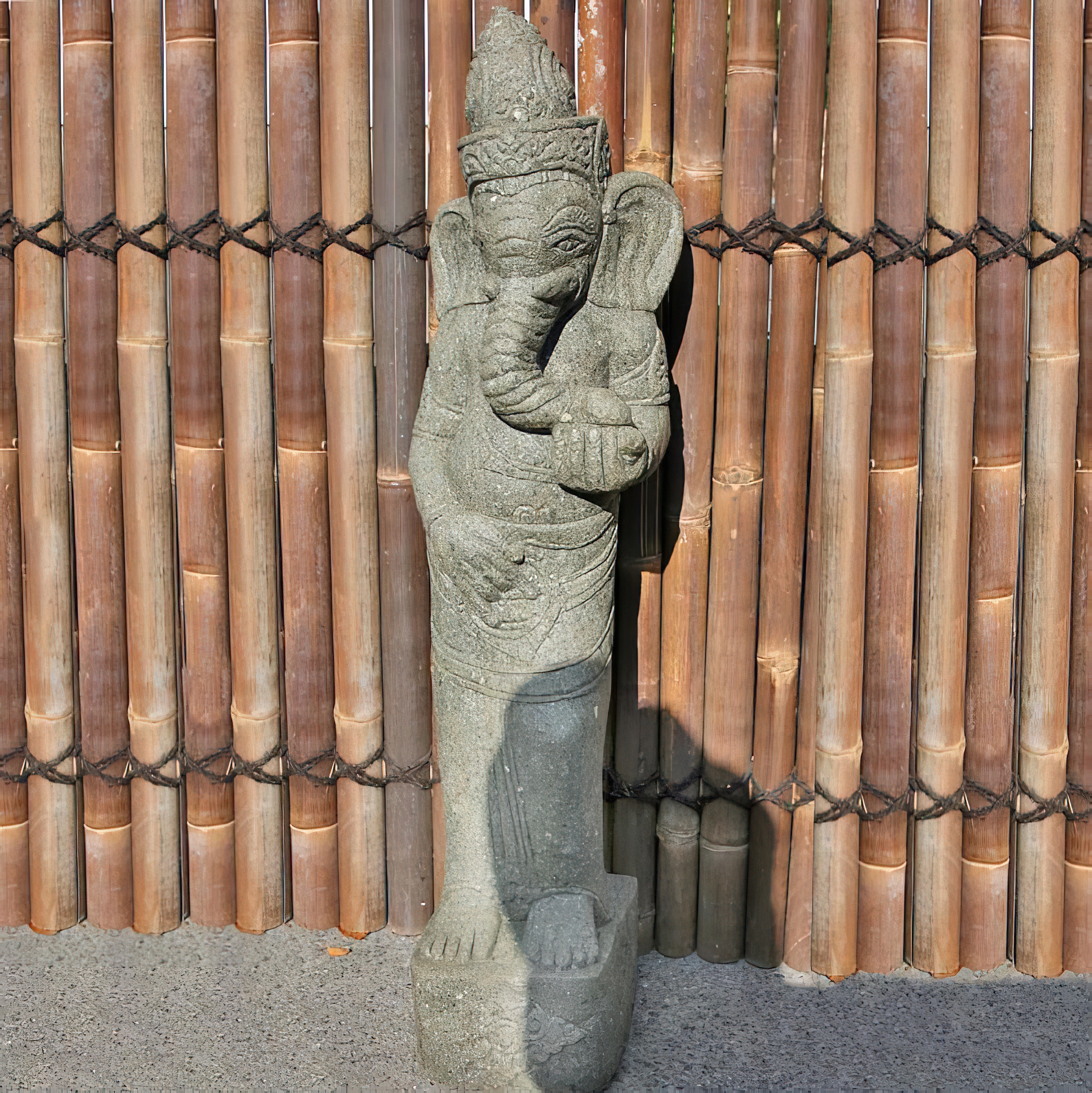 Statue en pierre de Ganesha avec une clôture en bambou en arrière-plan, parfaite pour une décoration de jardin exclusive