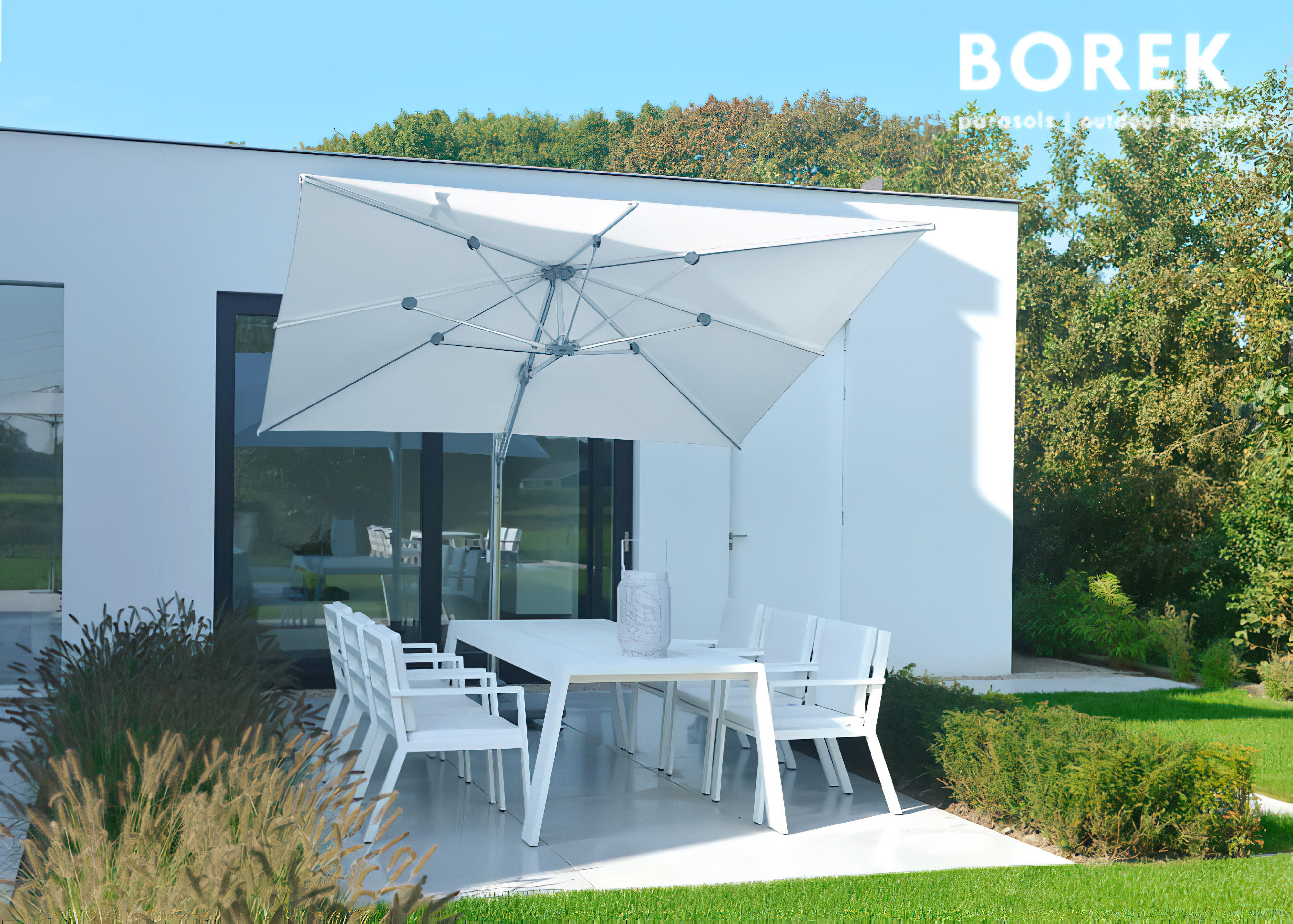 Weißer Gartentisch mit Stühlen und großem hellem Sonnenschirm vor modernem Haus