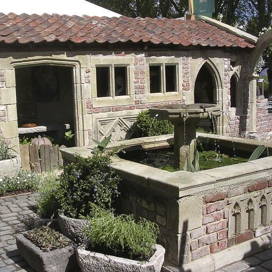 Fontaine de jardin en pierre avec bassin d'eau devant une maison en pierre