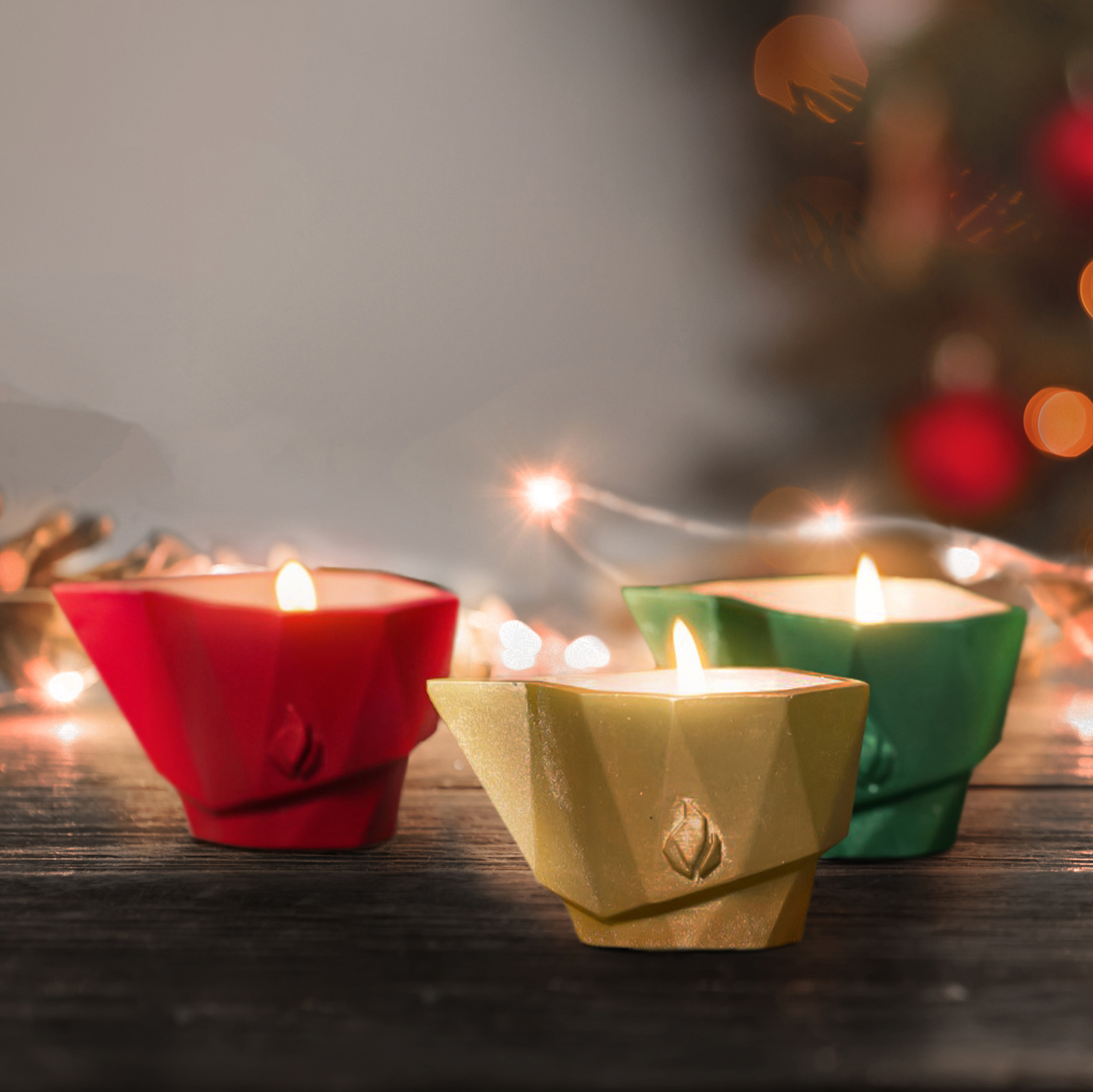 Tre candele da giardino accese in rosso, giallo e verde davanti a uno sfondo sfocato con decorazioni luminose