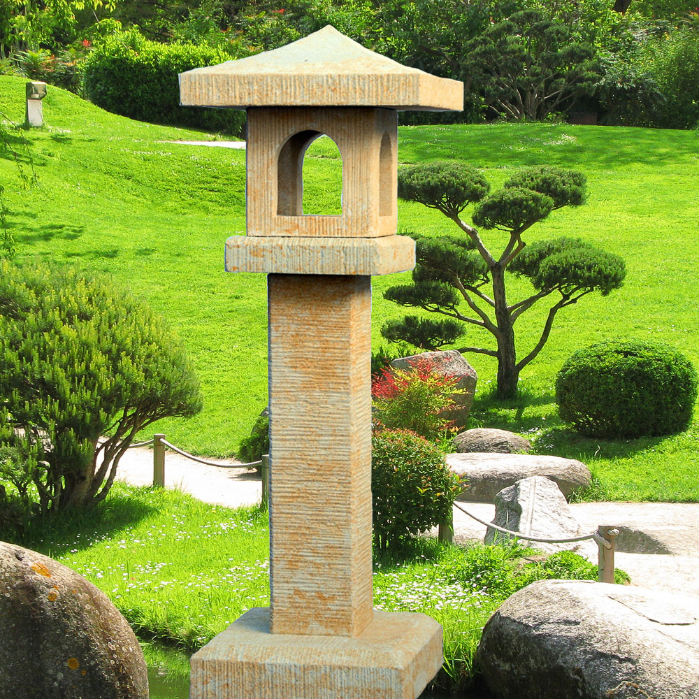 Lanterne en pierre beige dans un jardin bien entretenu avec des plantes vertes