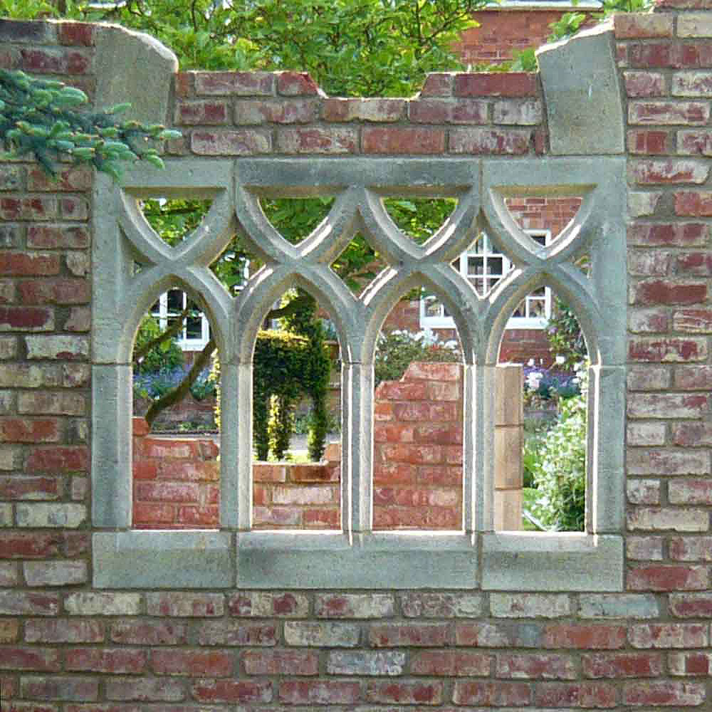 Antike Mauer mit gotischem Bogenfenster aus Stein, eingebettet in eine Gartenlandschaft