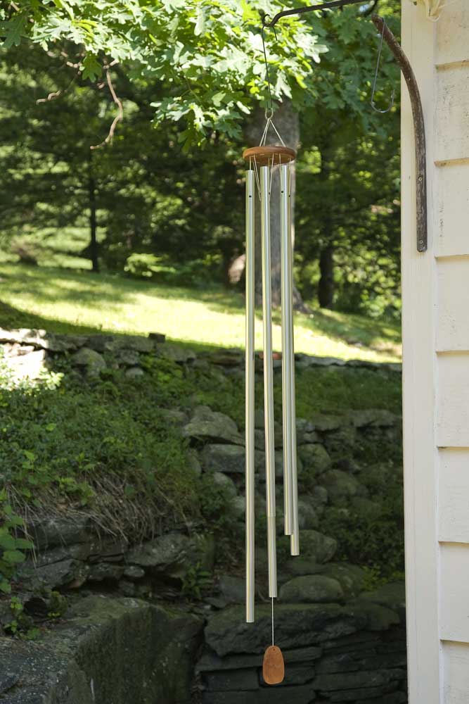 Campanello a vento con lunghe bacchette di metallo davanti a un giardino verde e un muro di casa