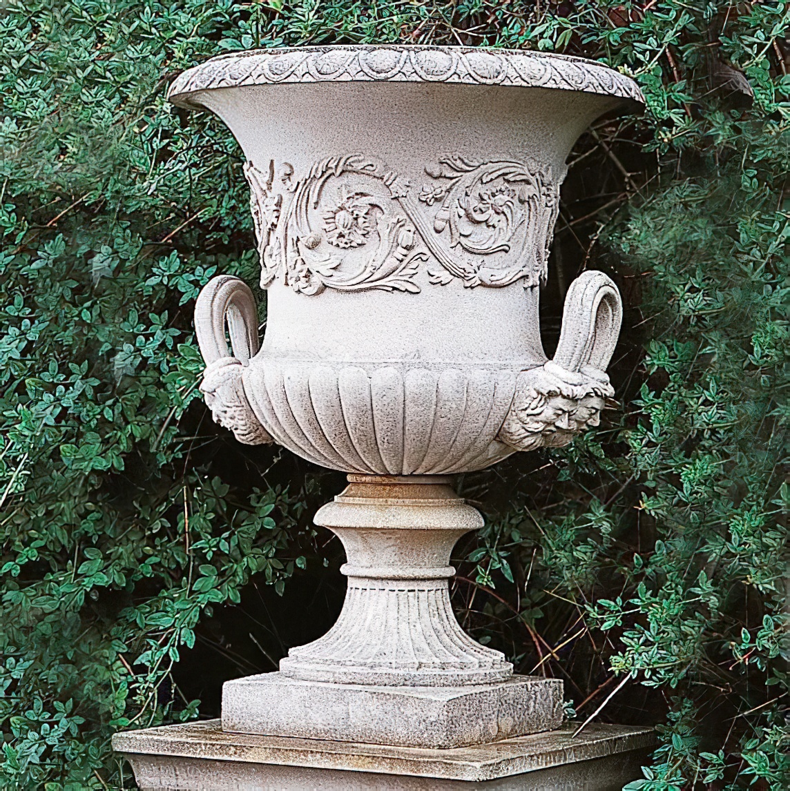 Grande vaso da giardino in pietra bianca decorato, davanti a cespugli verdi