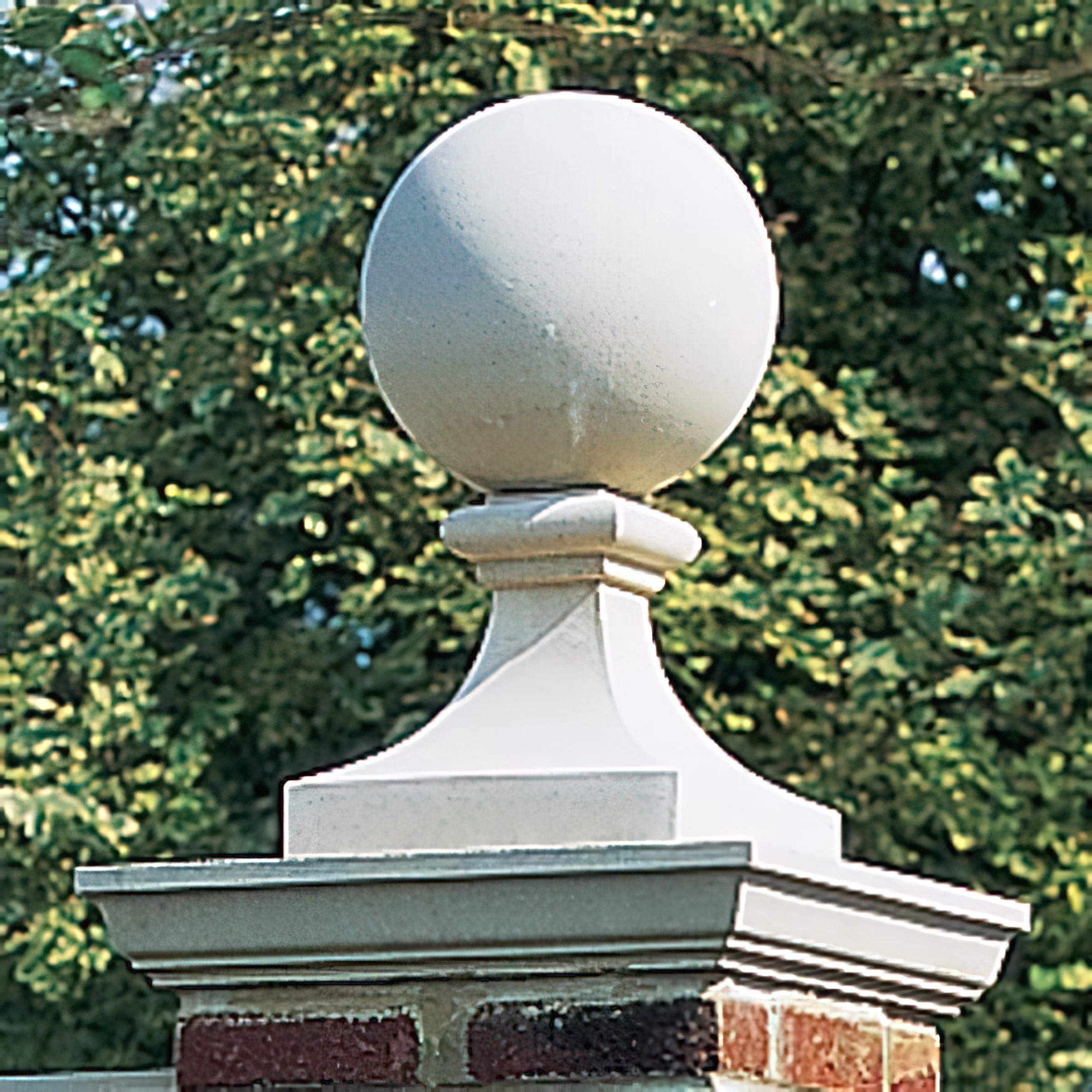 Sphère blanche en pierre comme décoration de jardin sur un pilier en briques devant des buissons verts