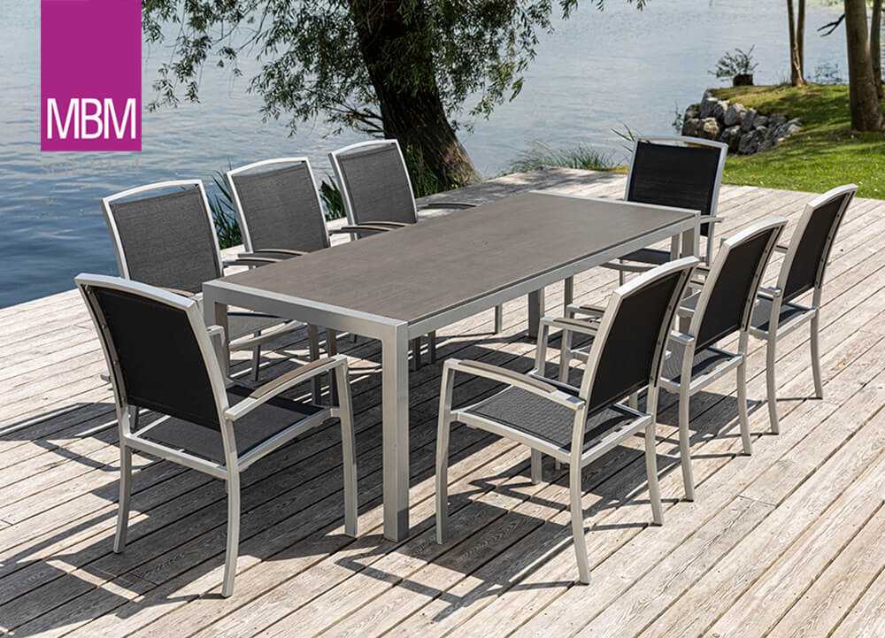 Table de jardin en métal avec huit chaises sur une terrasse en bois au bord du lac