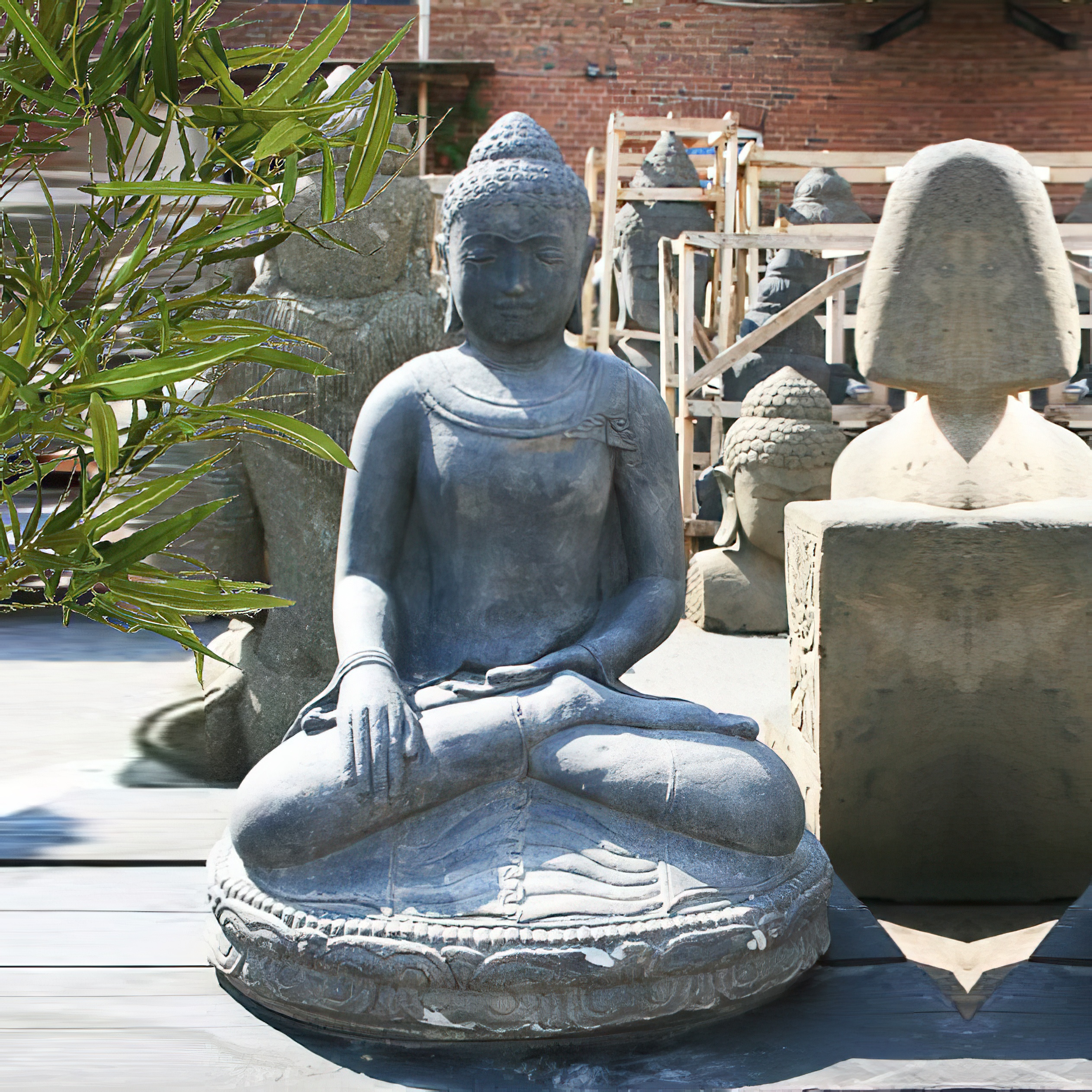 Grande statue de Bouddha assise en pierre entourée d'autres sculptures et plantes de jardin
