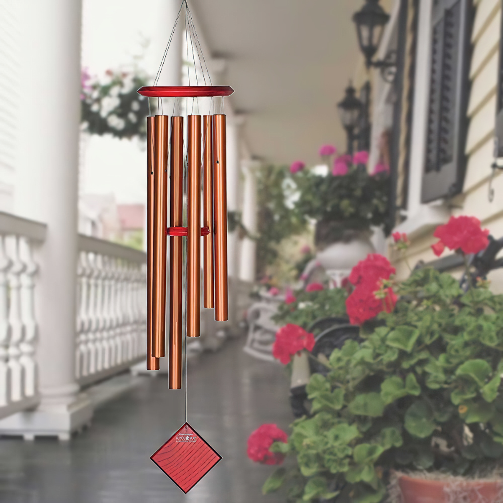 Carillon éolien en cuivre suspendu sur une véranda avec des fleurs en arrière-plan