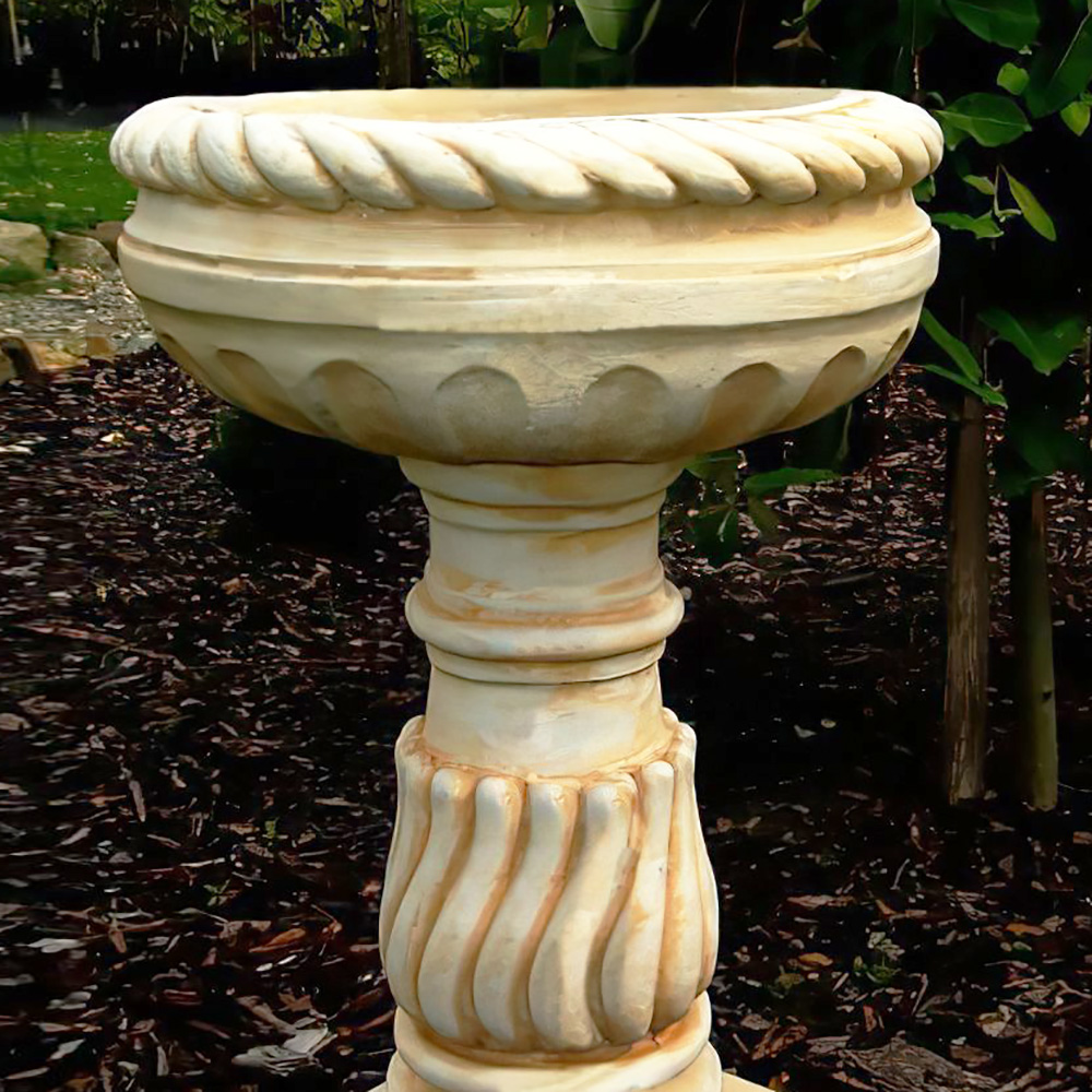 Abbeveratoio in pietra con base decorativa a spirale posizionato in giardino