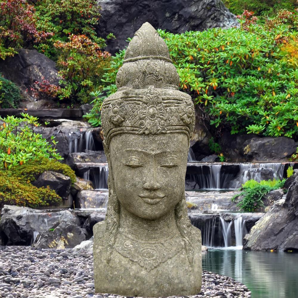 Grande scultura in pietra di Buddha davanti a una cascata a più livelli in un giardino verde