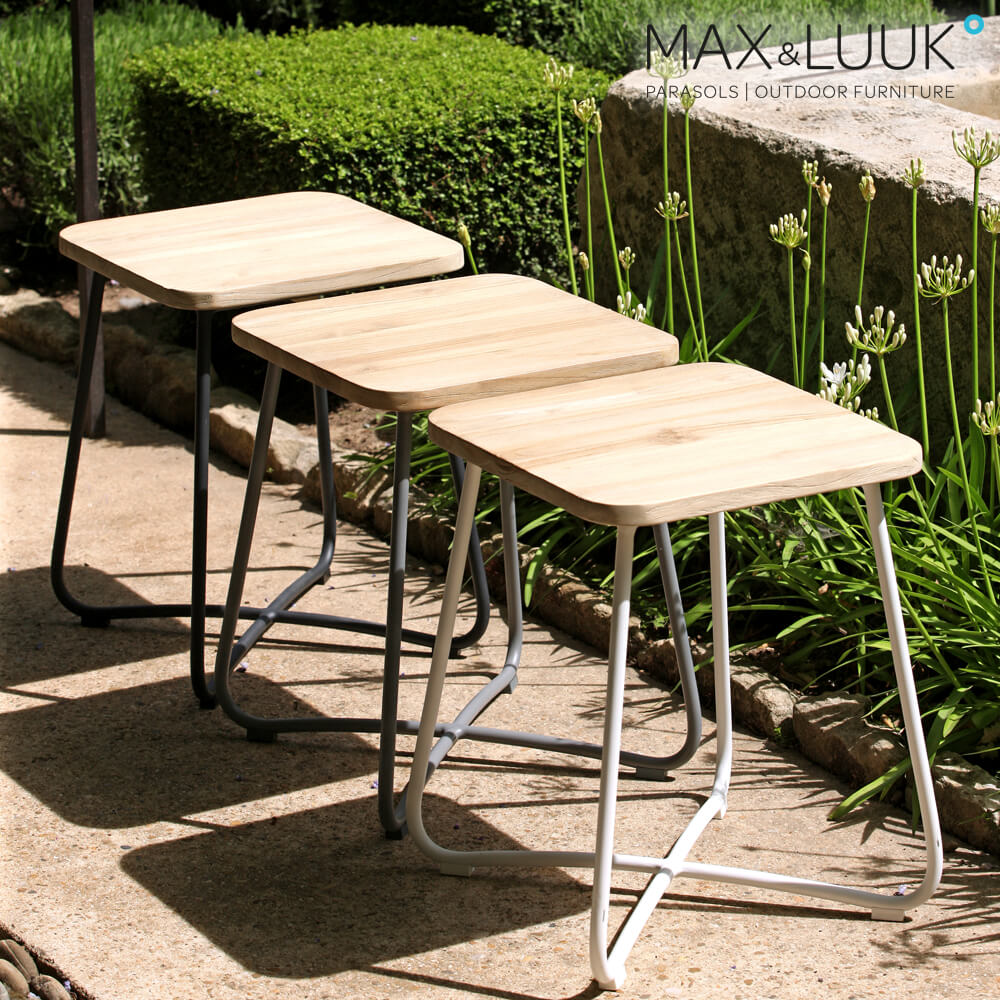 Tre tavoli da giardino moderni in legno con struttura metallica su una terrazza circondata da piante da giardino
