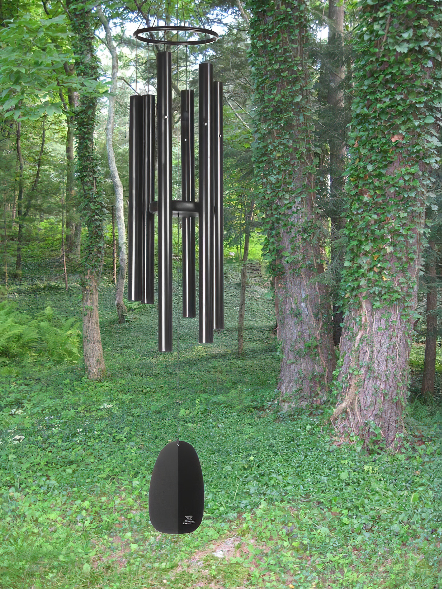 Grandi campane a vento con tubi neri appese a un albero in una foresta verde coperta di muschio