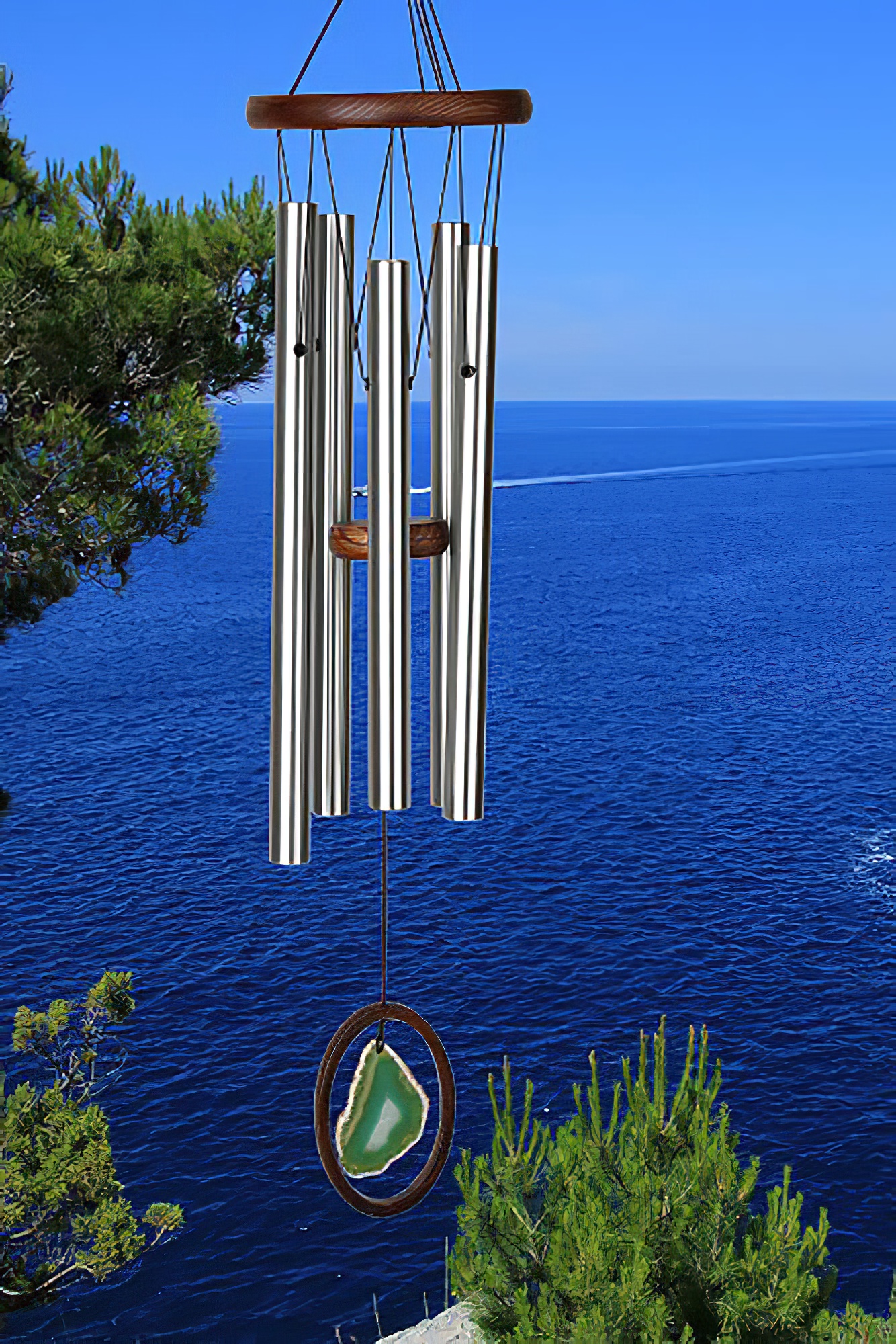 Carillon à vent en métal avec tubes sonores devant la mer bleue et un arbre vert