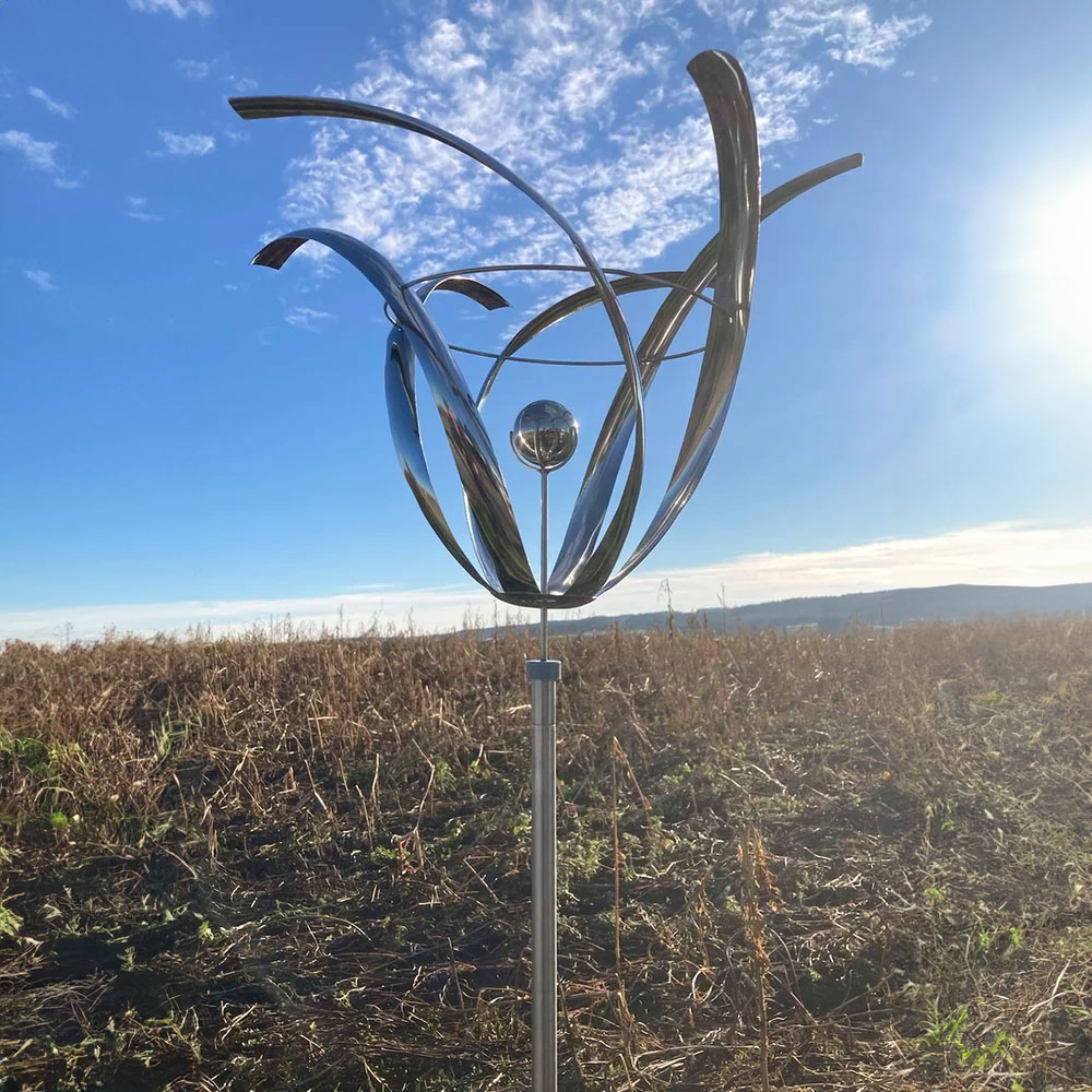 Stele da giardino astratta in acciaio inox con sfera davanti a cielo blu e campo