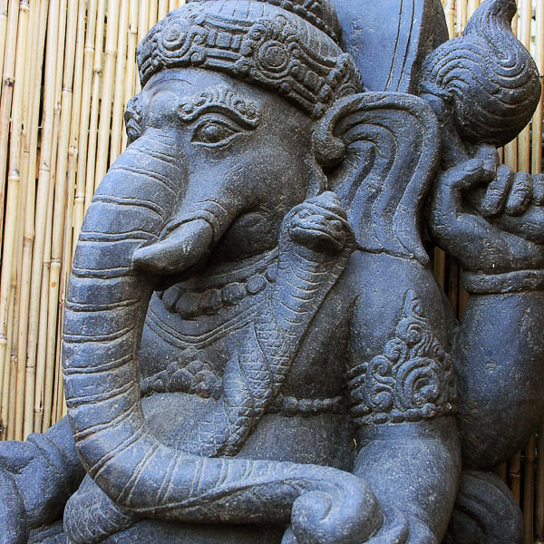 Gros plan d'une statue en pierre représentant un éléphant avec des sculptures détaillées devant un mur en bambou