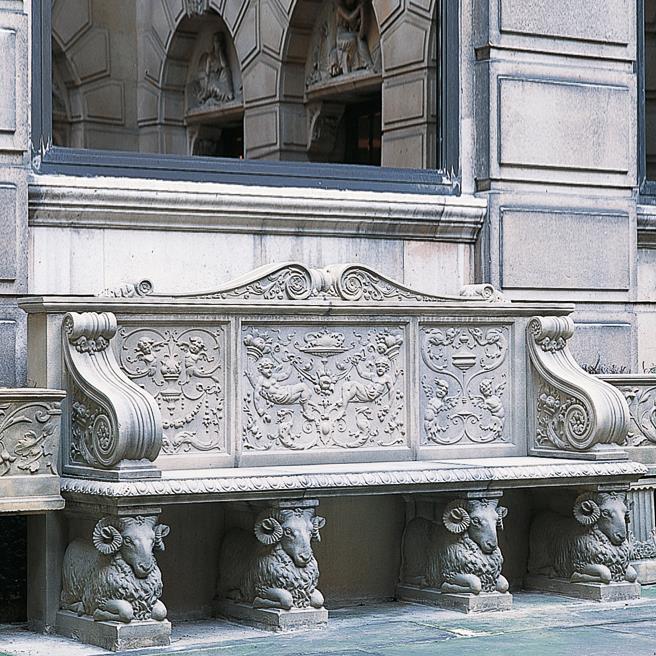 Panchina in pietra scolpita con dettagli decorativi davanti a una facciata storica