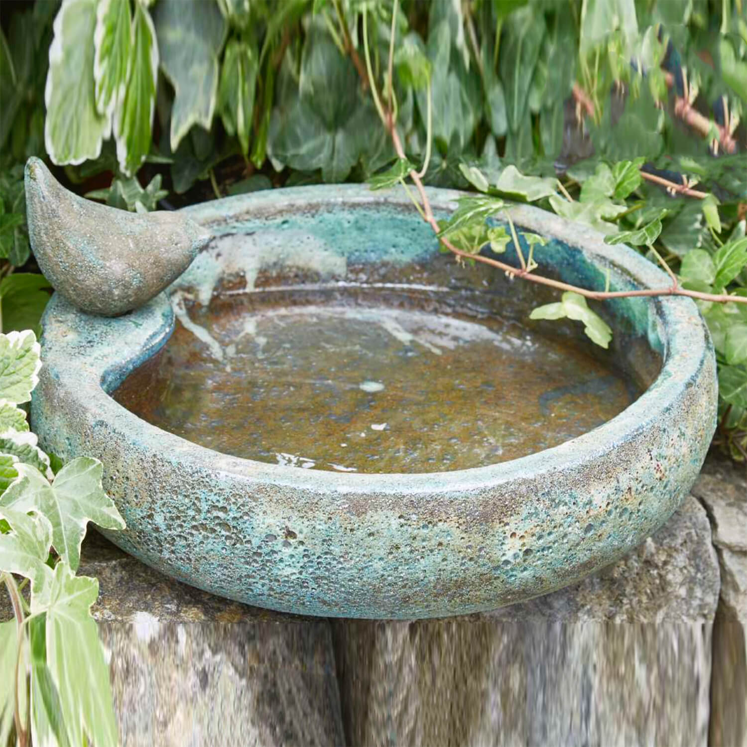 Abbeveratoio verde in rame con una figura decorativa di uccello sul bordo, posizionato nel giardino