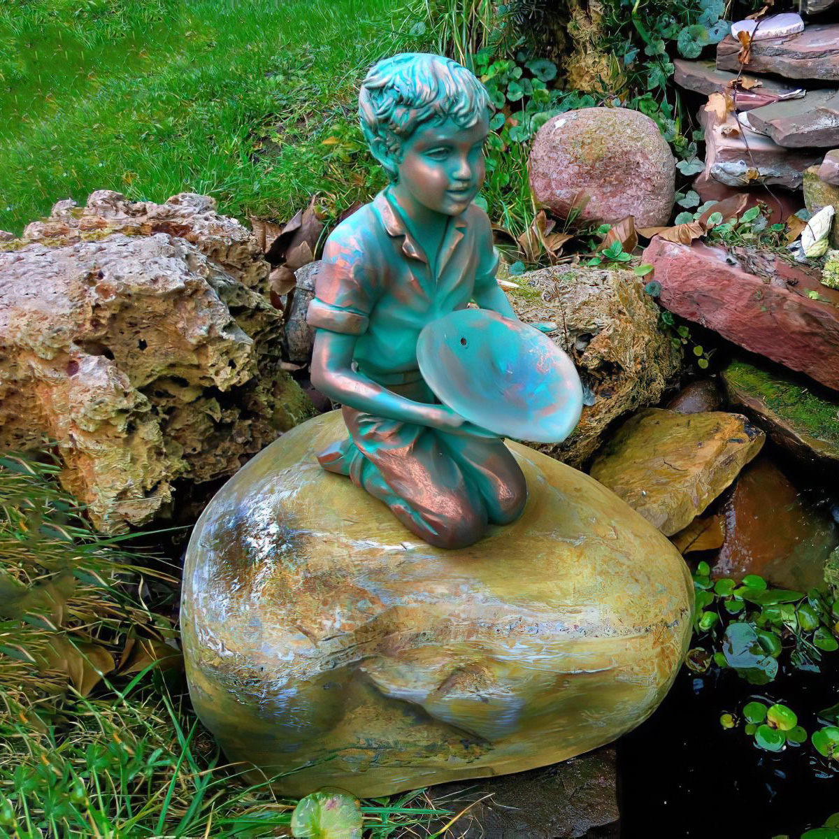 Sculpture en bronze d'un garçon tenant un bol, assis sur une grande pierre dans un jardin près d'un étang