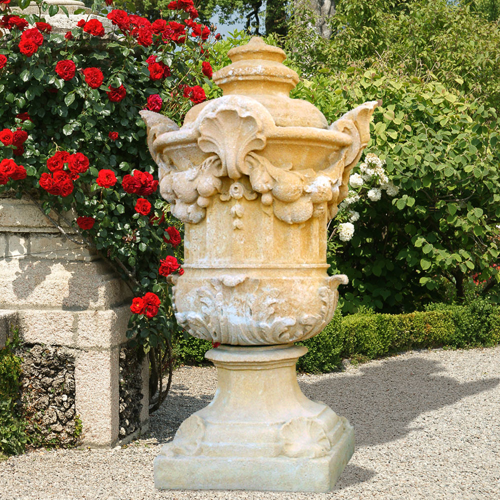 Fontaine de jardin en pierre finement sculptée devant des roses rouges en fleurs