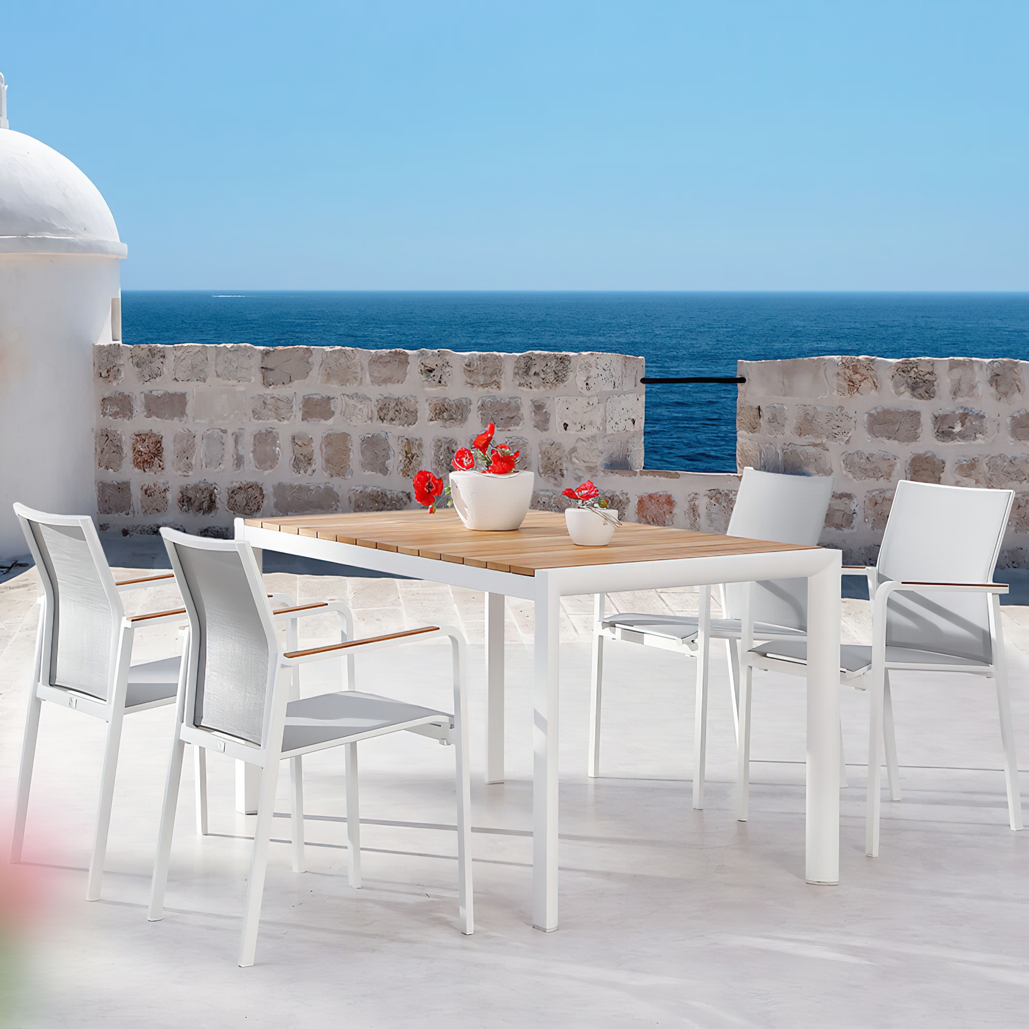 Table de jardin blanche avec plateau en bois et quatre chaises blanches sur une terrasse avec vue sur la mer