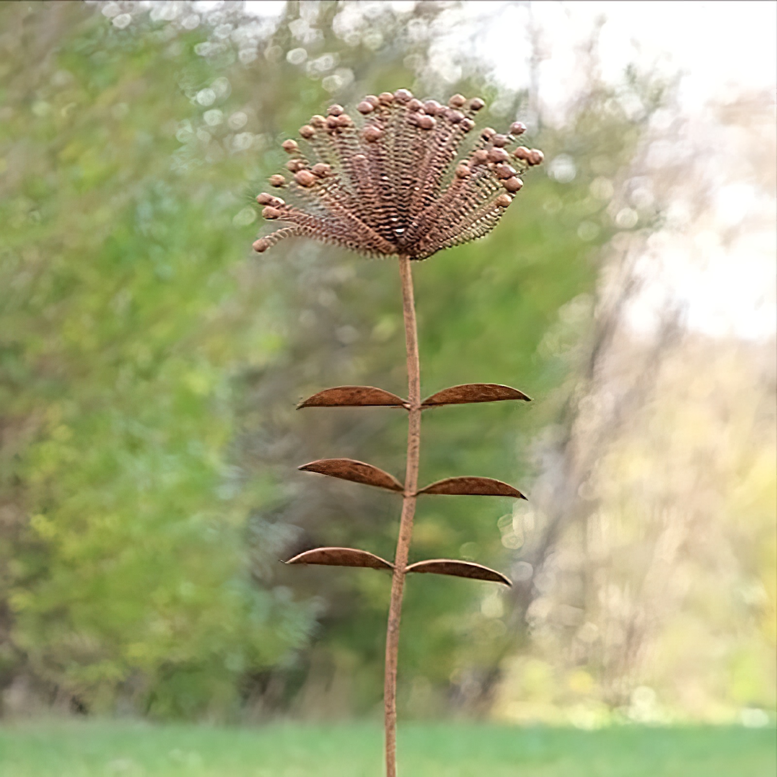 Rostiger Metall-Gartenstecker in Form einer stilisierten Blume mit Blättern im Garten