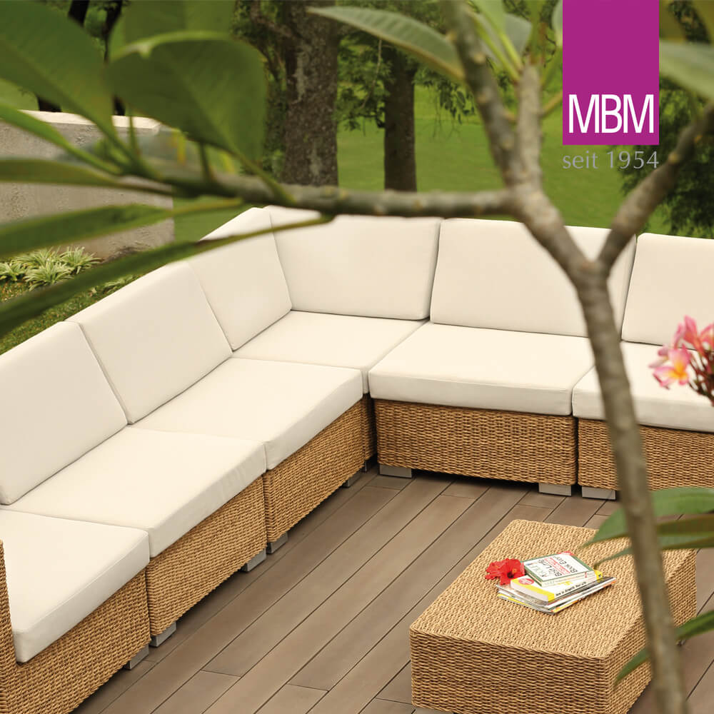 Weisses Gartensofa mit Rattanstruktur auf Holzterrasse umgeben von Pflanzen