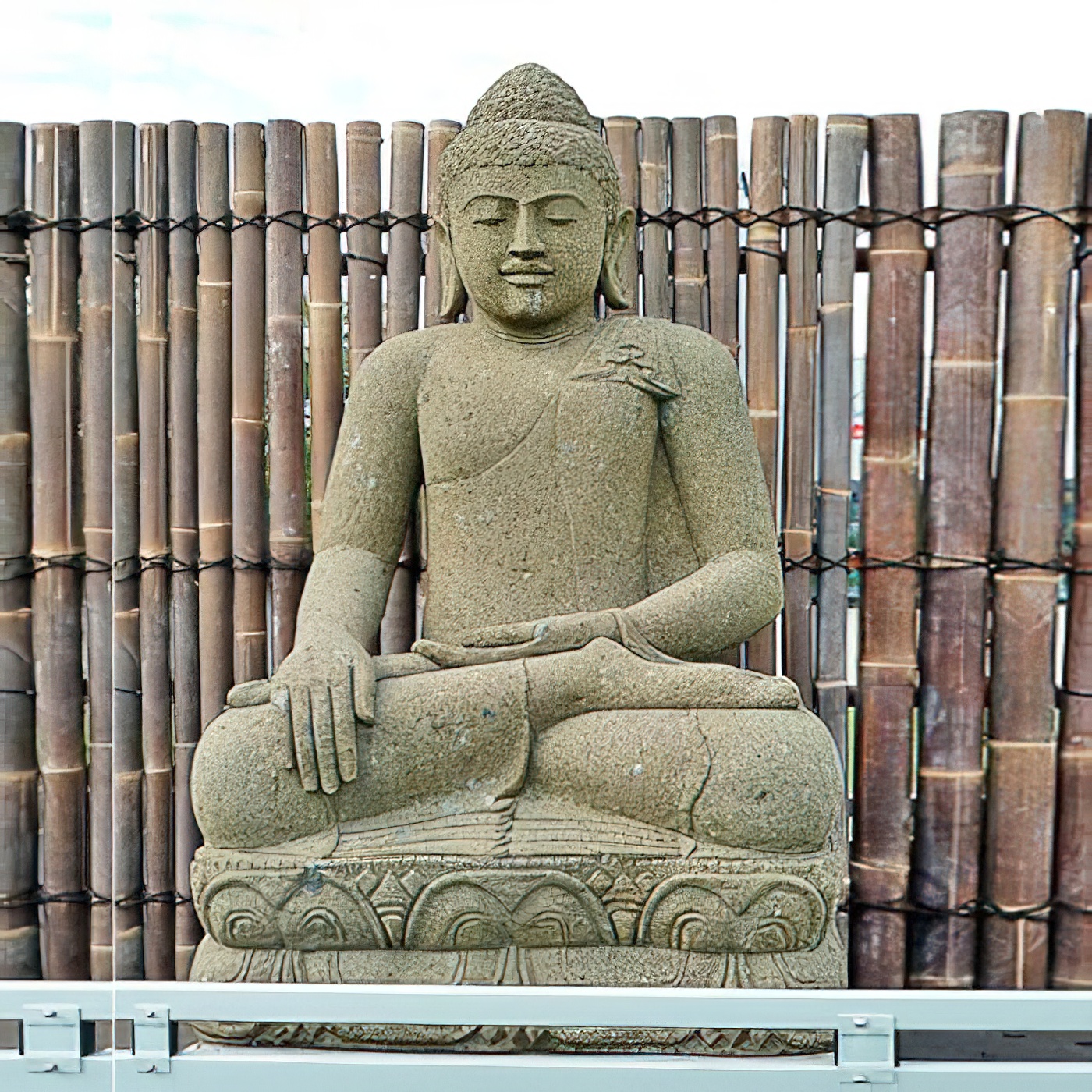 Stein Buddha Statue sitzend vor Bambuszaun als Gartendekoration