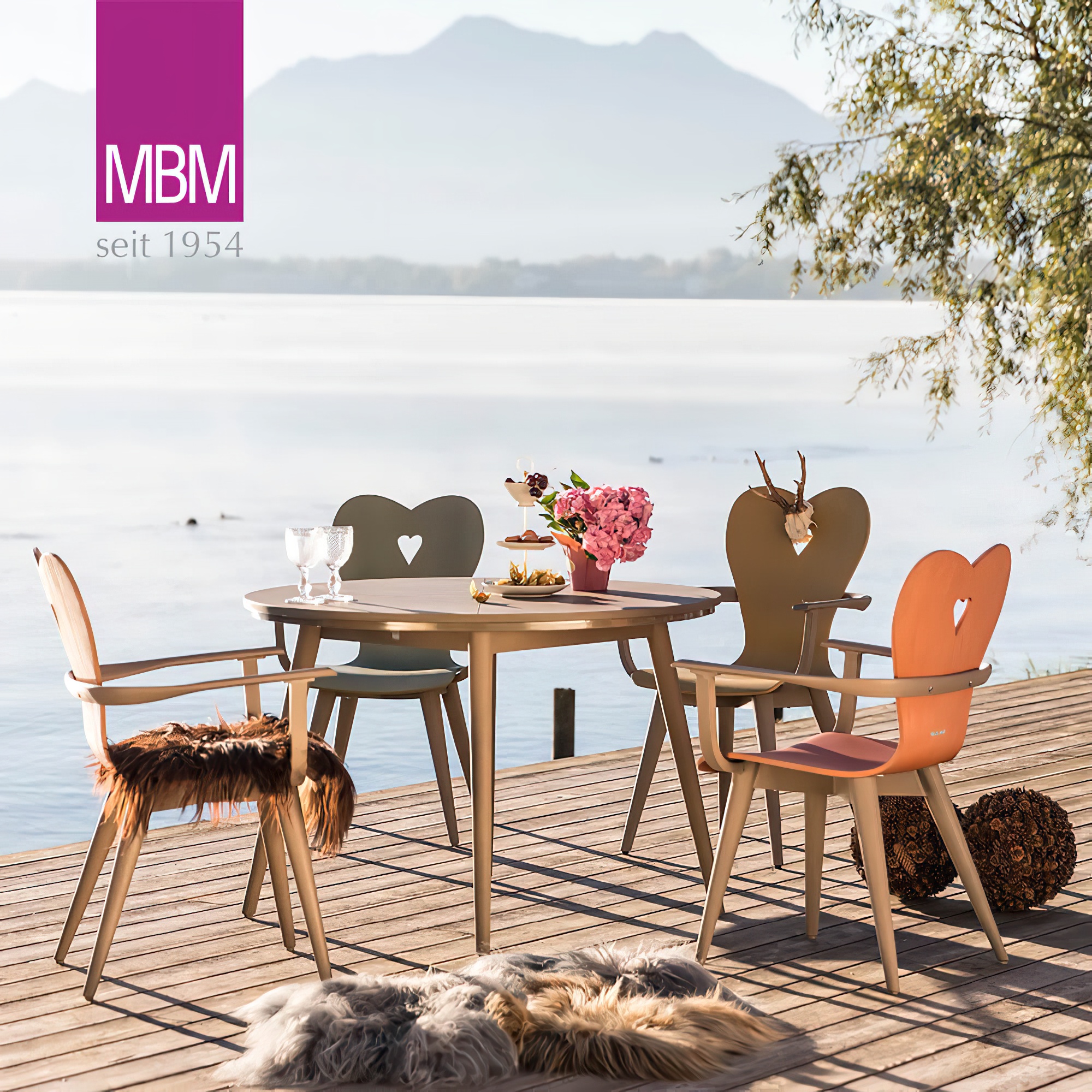 Table en bois avec quatre chaises de jardin décoratives sur une terrasse au bord de l'eau