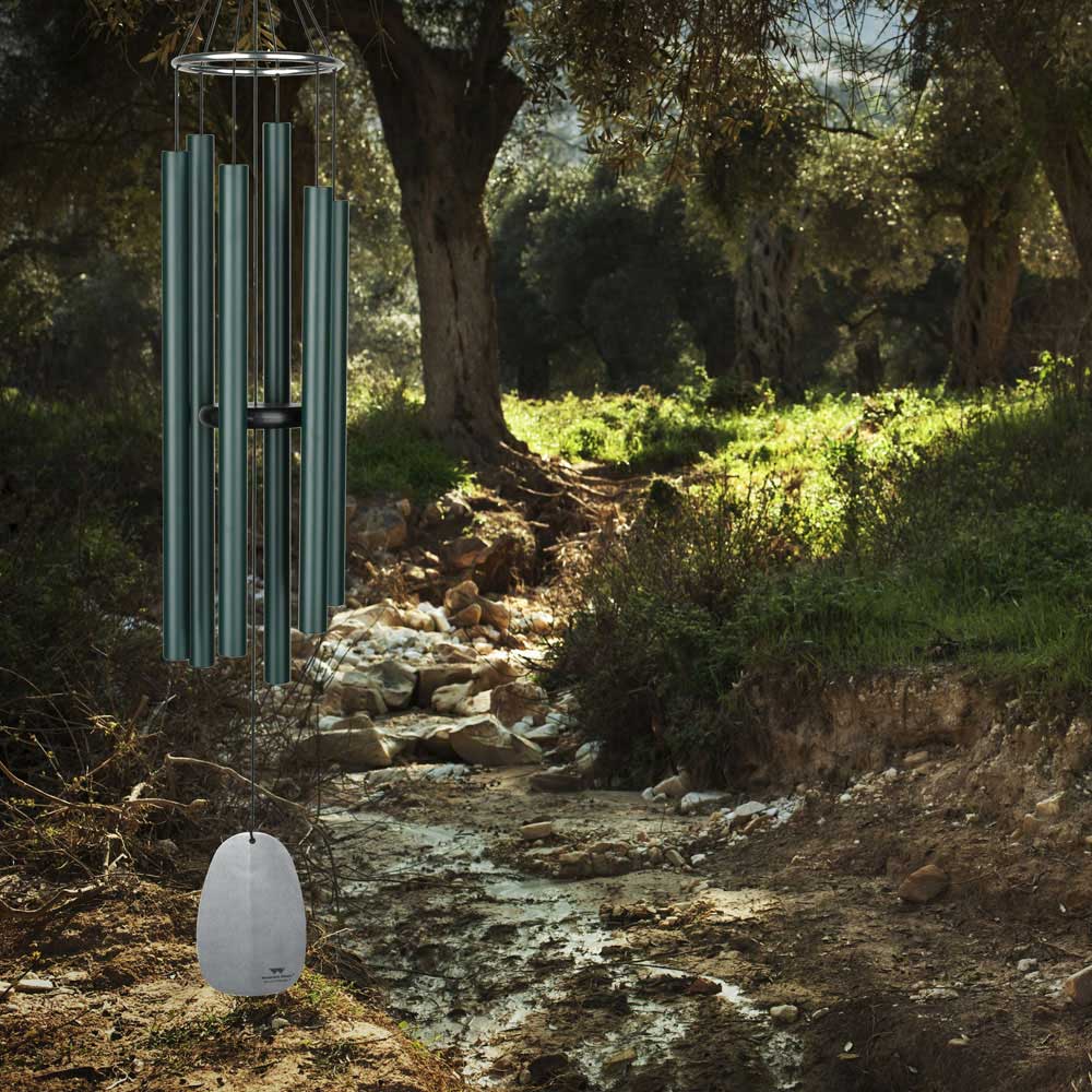 Carillon en métal suspendu au-dessus d'un ruisseau dans un jardin verdoyant avec des arbres