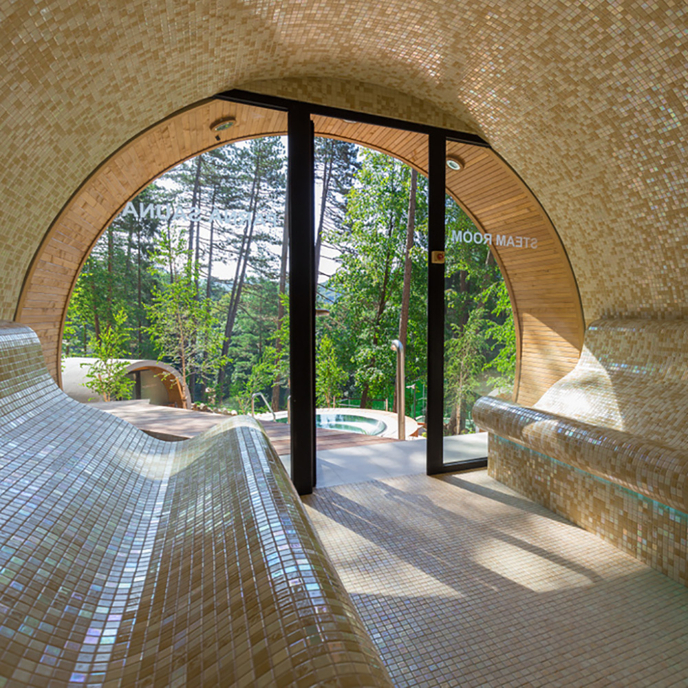 Interno di una spa con panchine a mosaico e ampia vetrata che si affaccia sul giardino