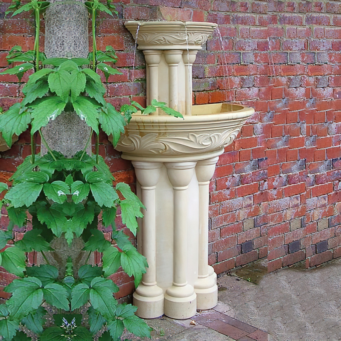 Fontana da giardino in pietra con design a colonne davanti a muro di mattoni e pianta rampicante verde