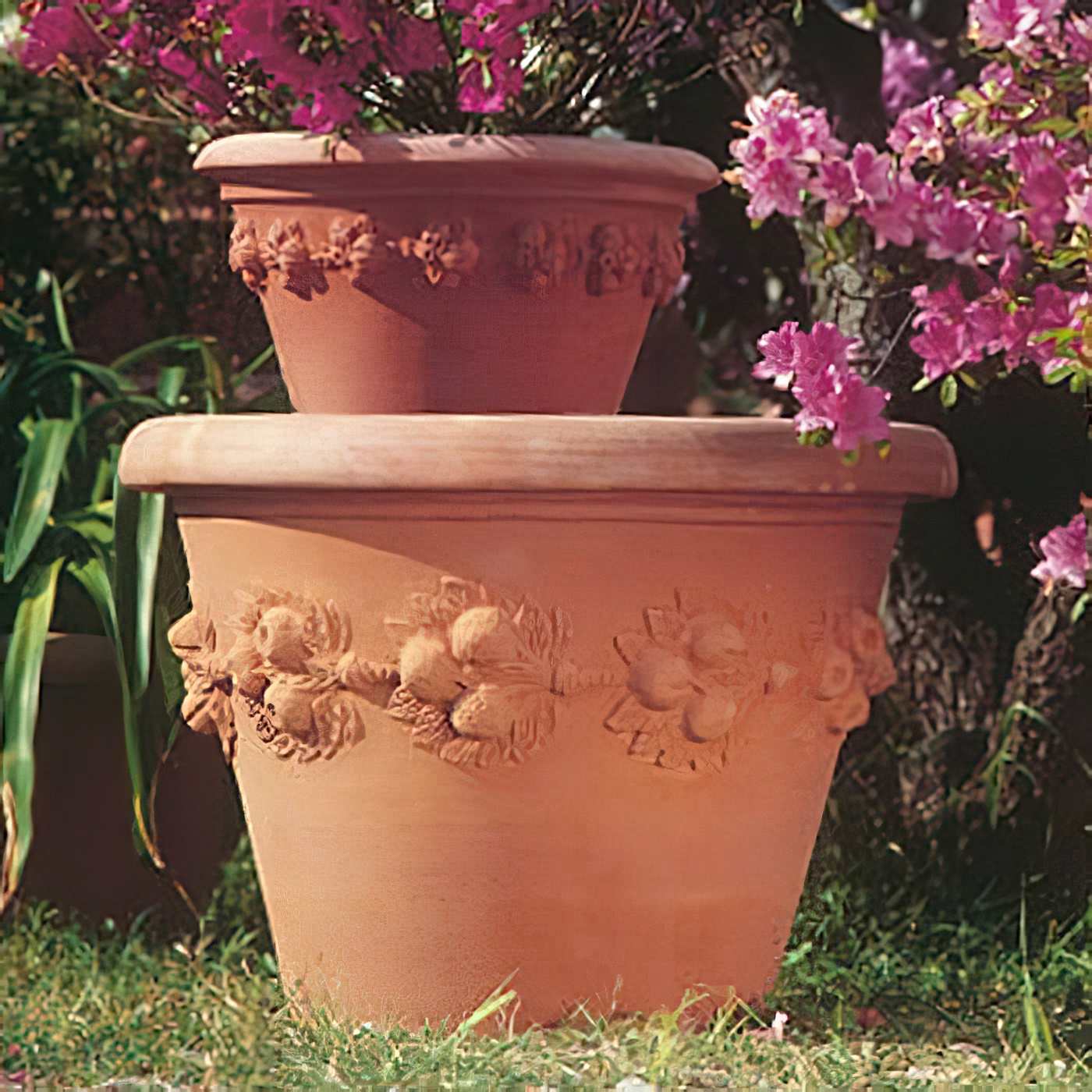 Deux pots de fleurs en terre cuite empilés avec des motifs floraux, entourés de plantes en fleurs dans le jardin