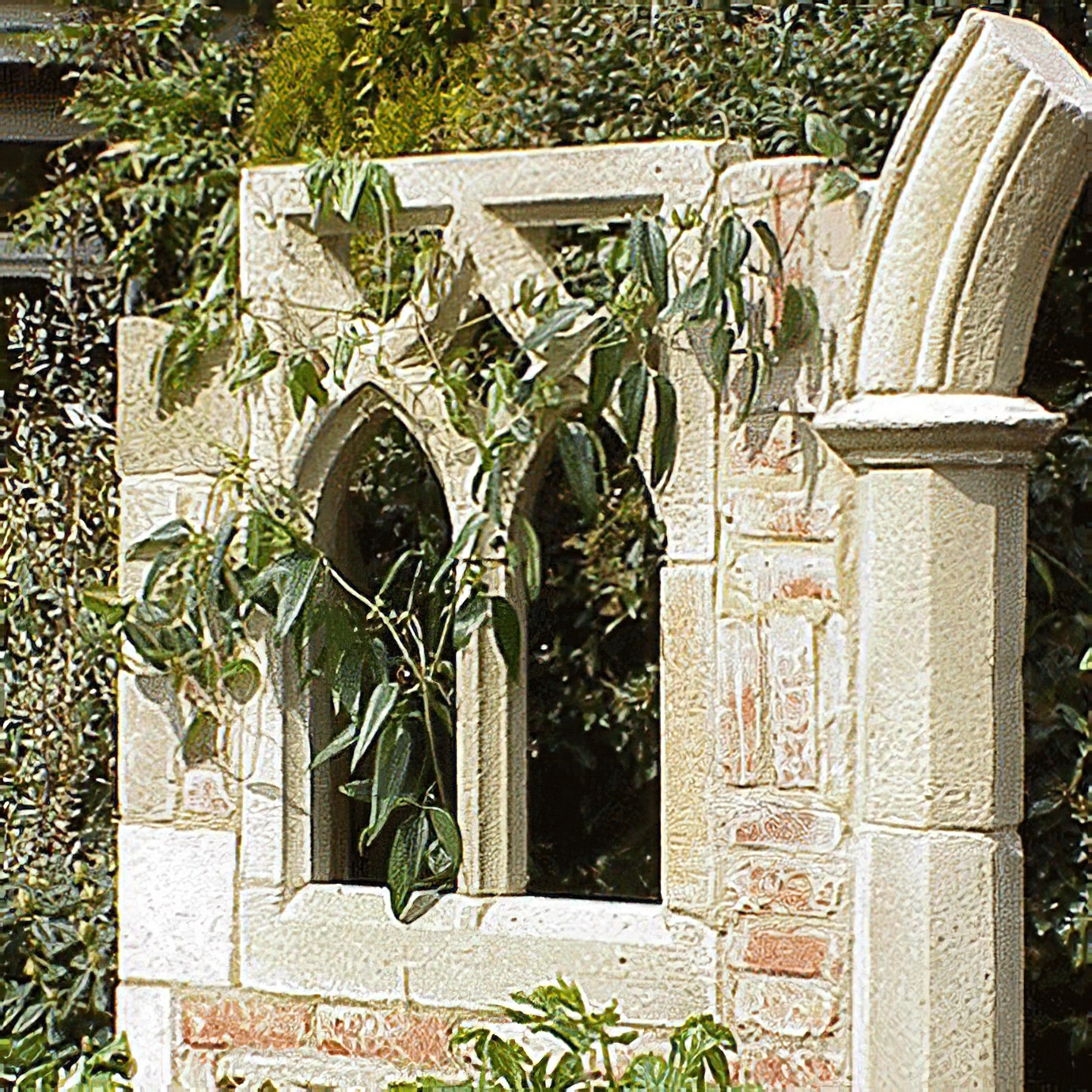 Gartendeko aus Stein mit gotischem Fenster und Kletterpflanze im Garten