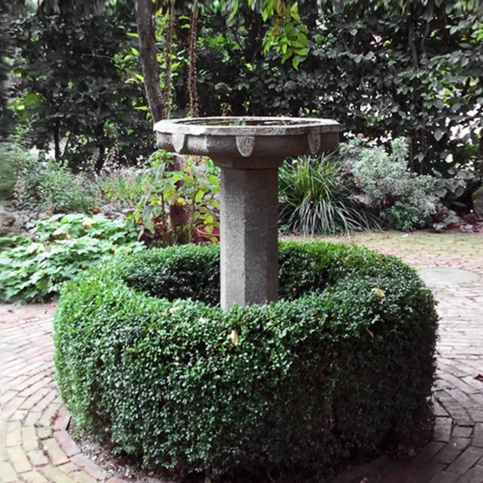 Meridiana in pietra grigia circondata da una siepe di bosso potata a forma rotonda nel giardino