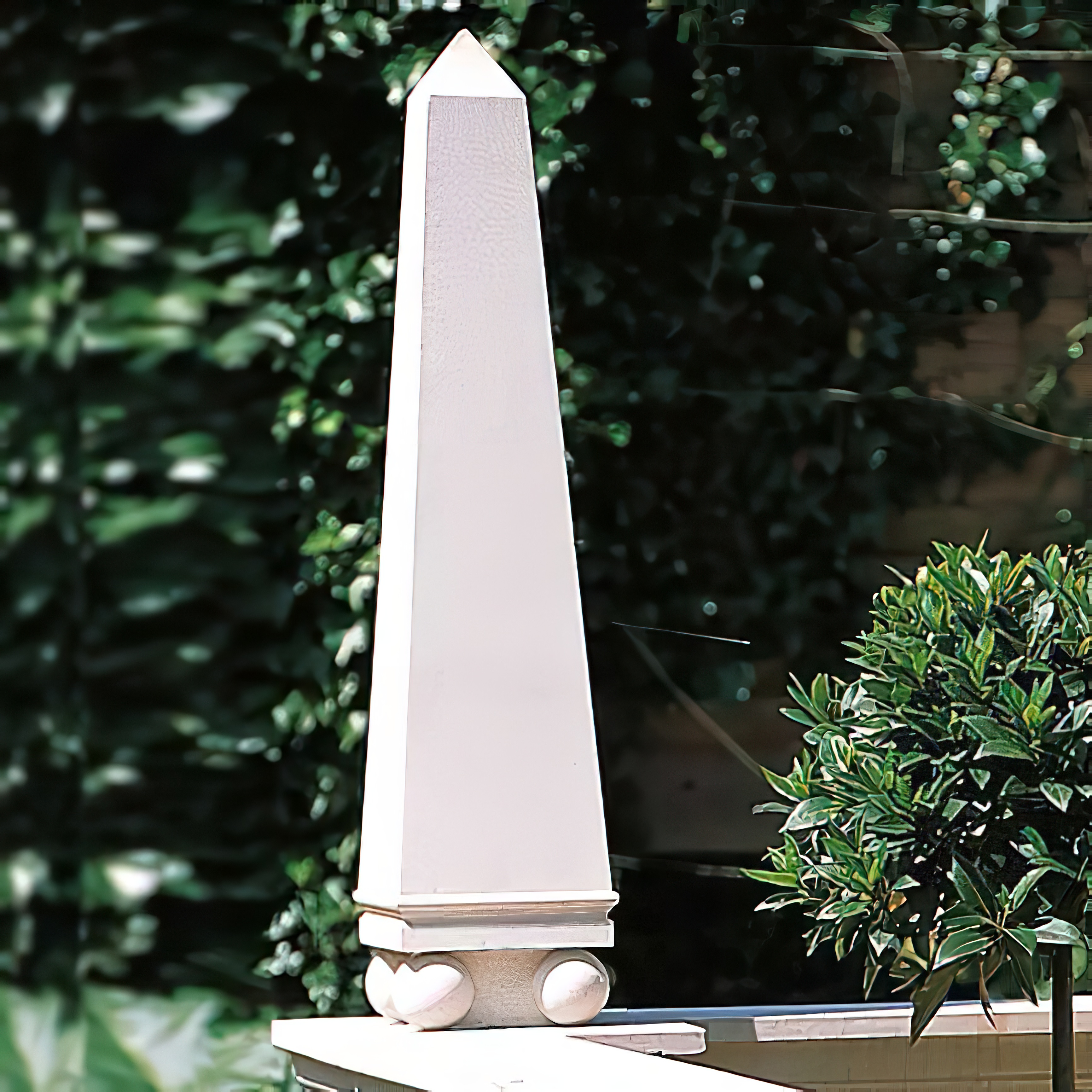 Weißer Steinobelisk als Gartendekoration neben grünem Pflanzenbusch
