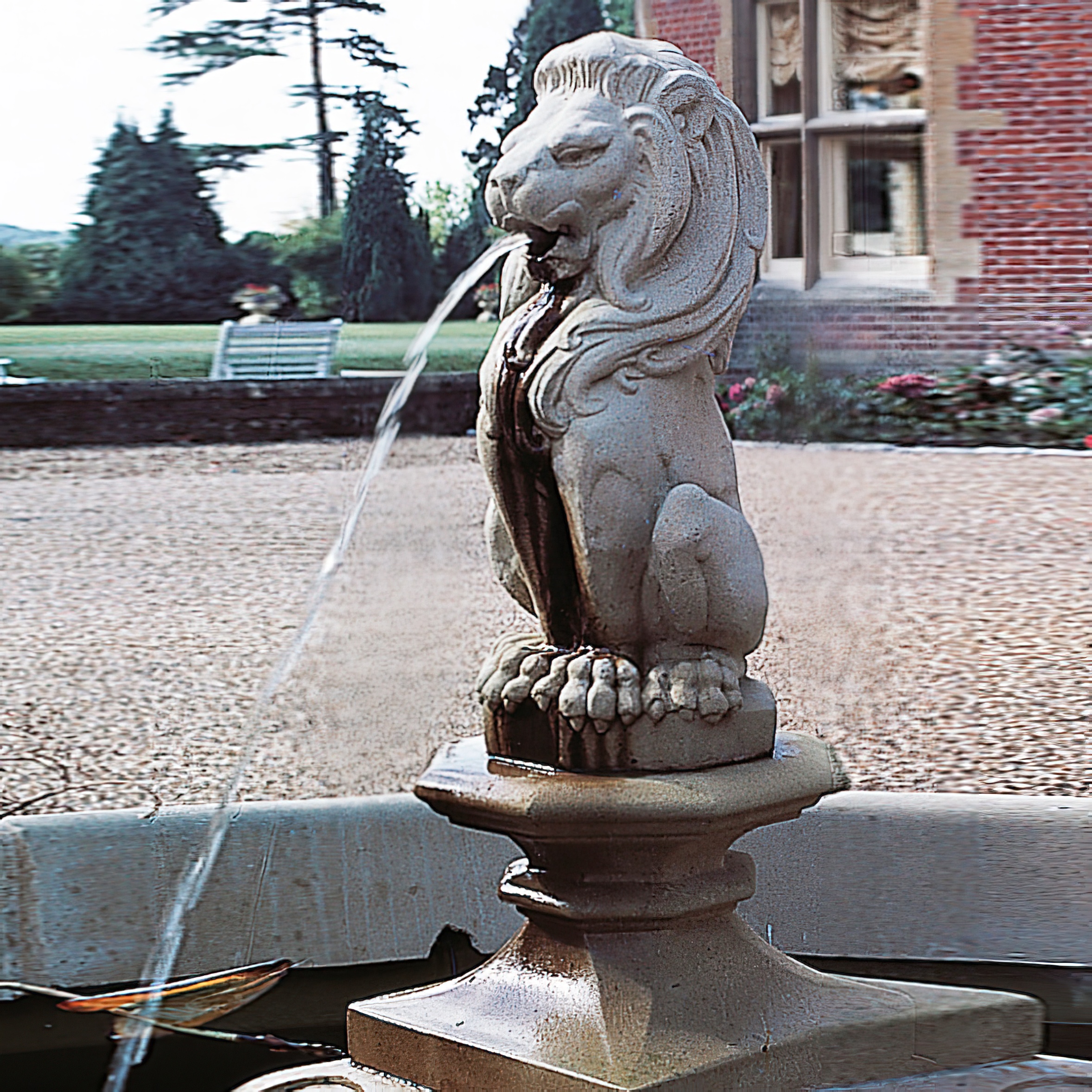 Steinerner Löwe mit Wasser, dekorativer Gartenbrunnen vor einem Gartenhintergrund