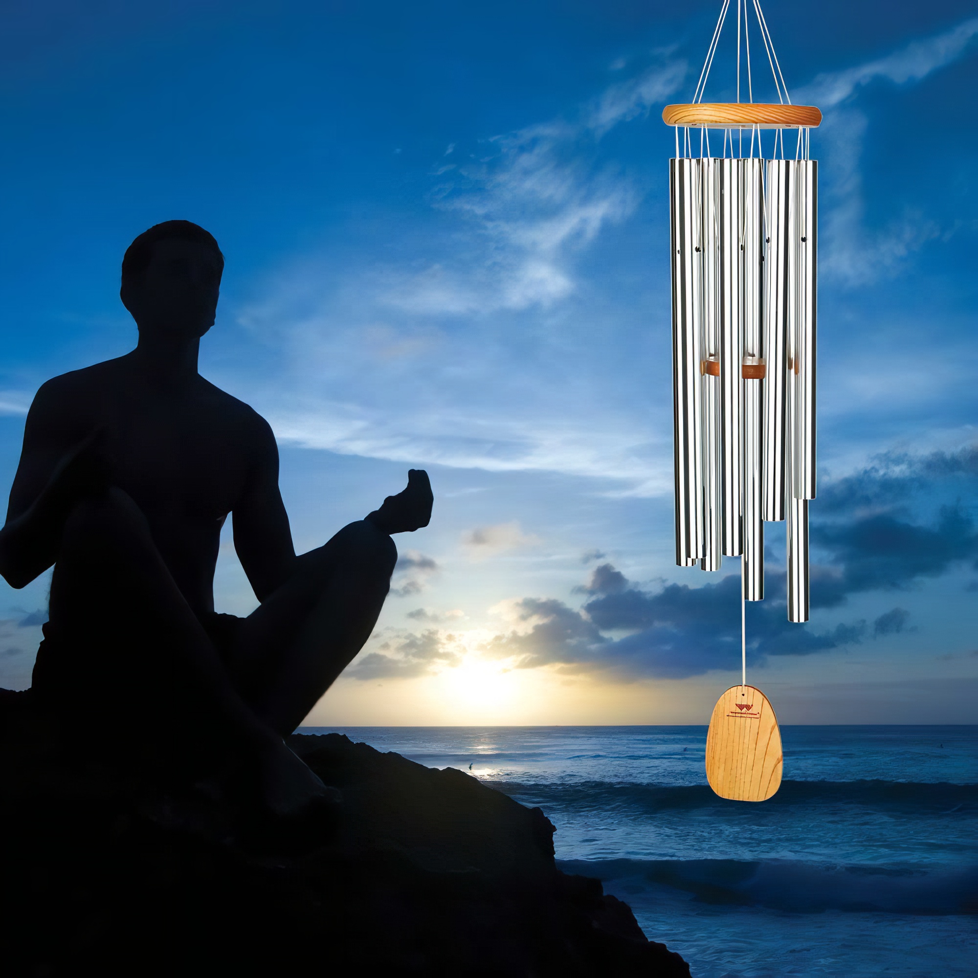 Sagoma di persona che medita accanto a un campanello a vento appeso sullo sfondo del mare al tramonto