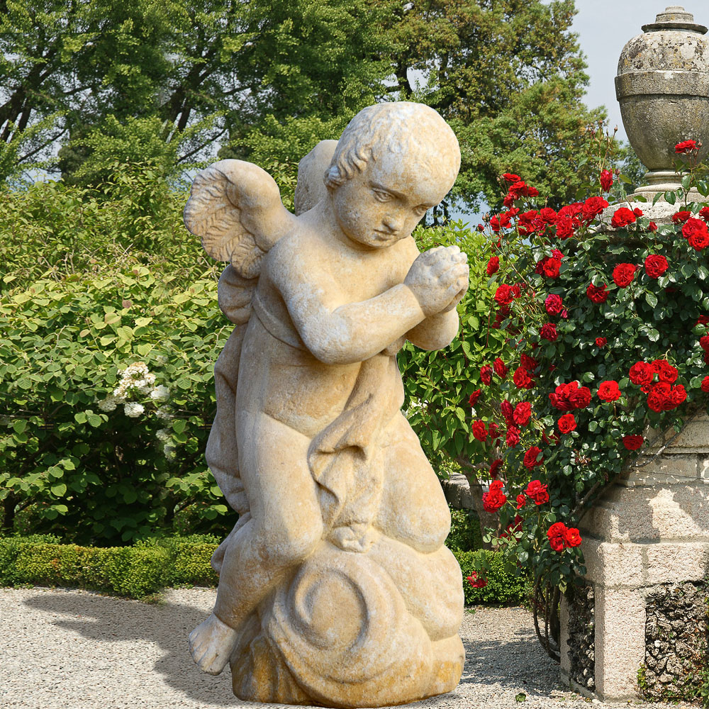 Angelo di pietra con mani giunte in un giardino fiorito con rose rosse