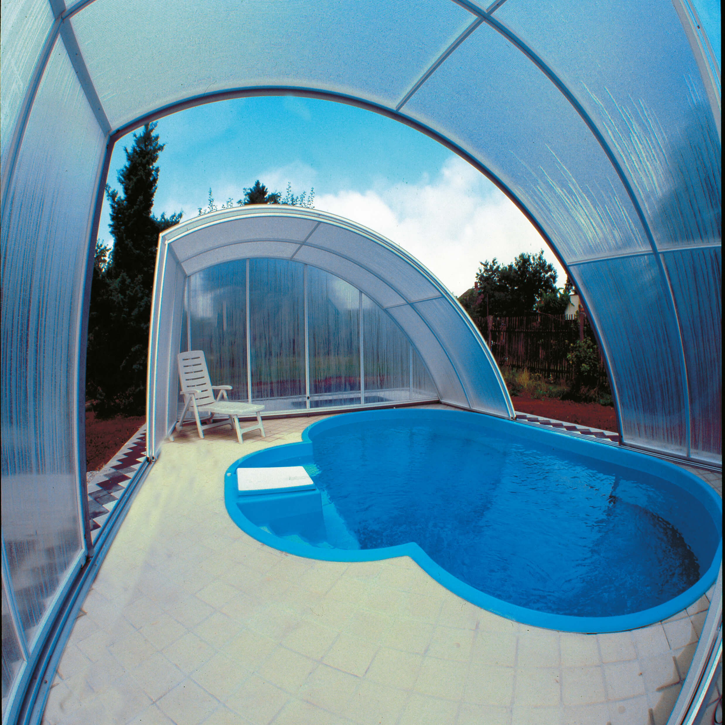Couverture transparente au-dessus d'une piscine bleue et chaise longue dans le jardin