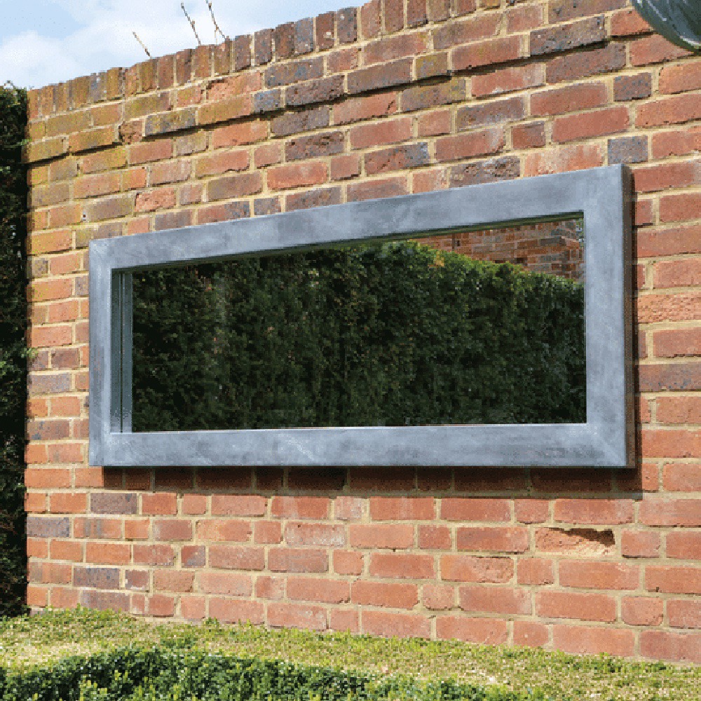 Grand miroir rectangulaire avec cadre gris fixé à un mur en briques dans un jardin