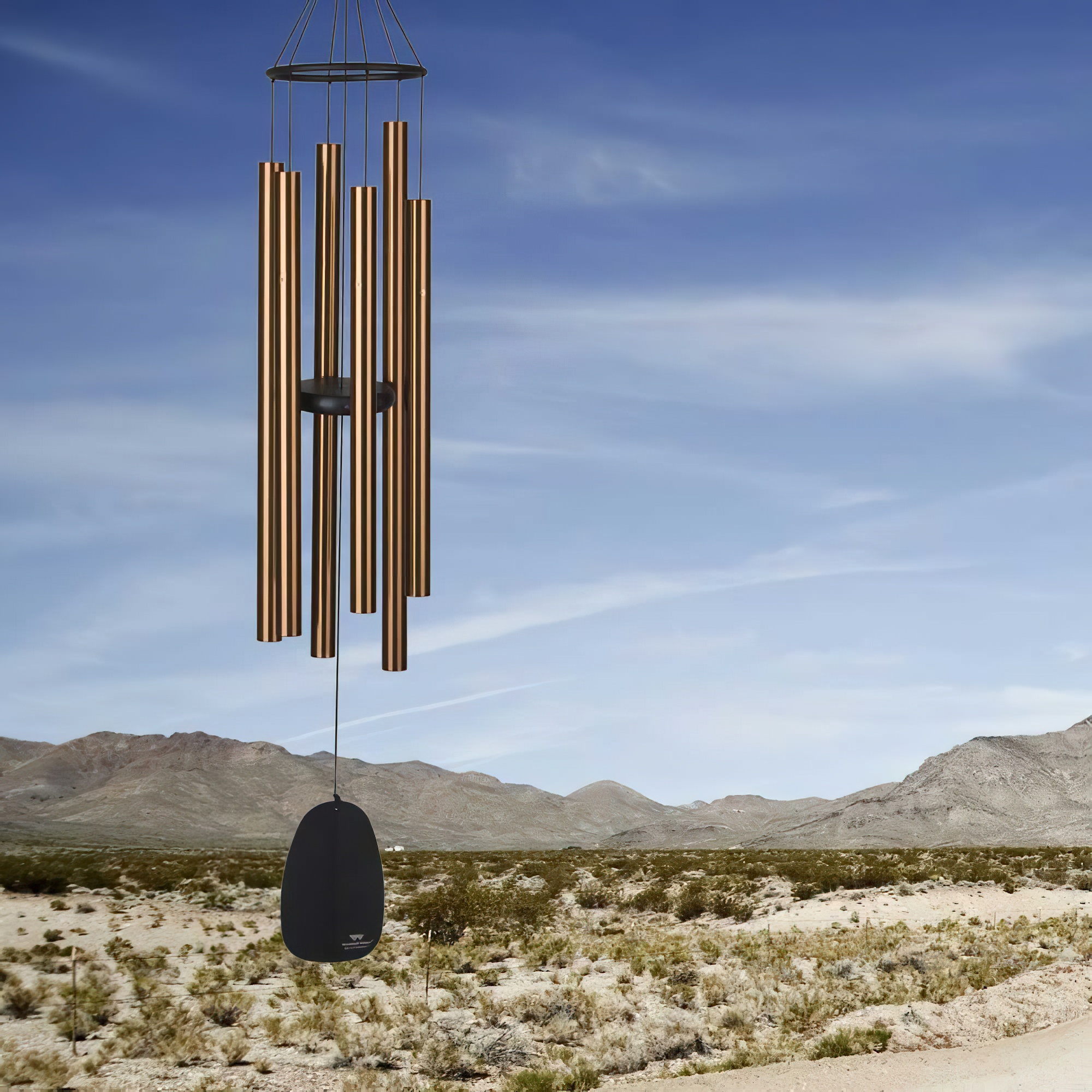 Grand carillon éolien avec tubes métalliques devant un paysage de désert et montagnes, décoration de jardin
