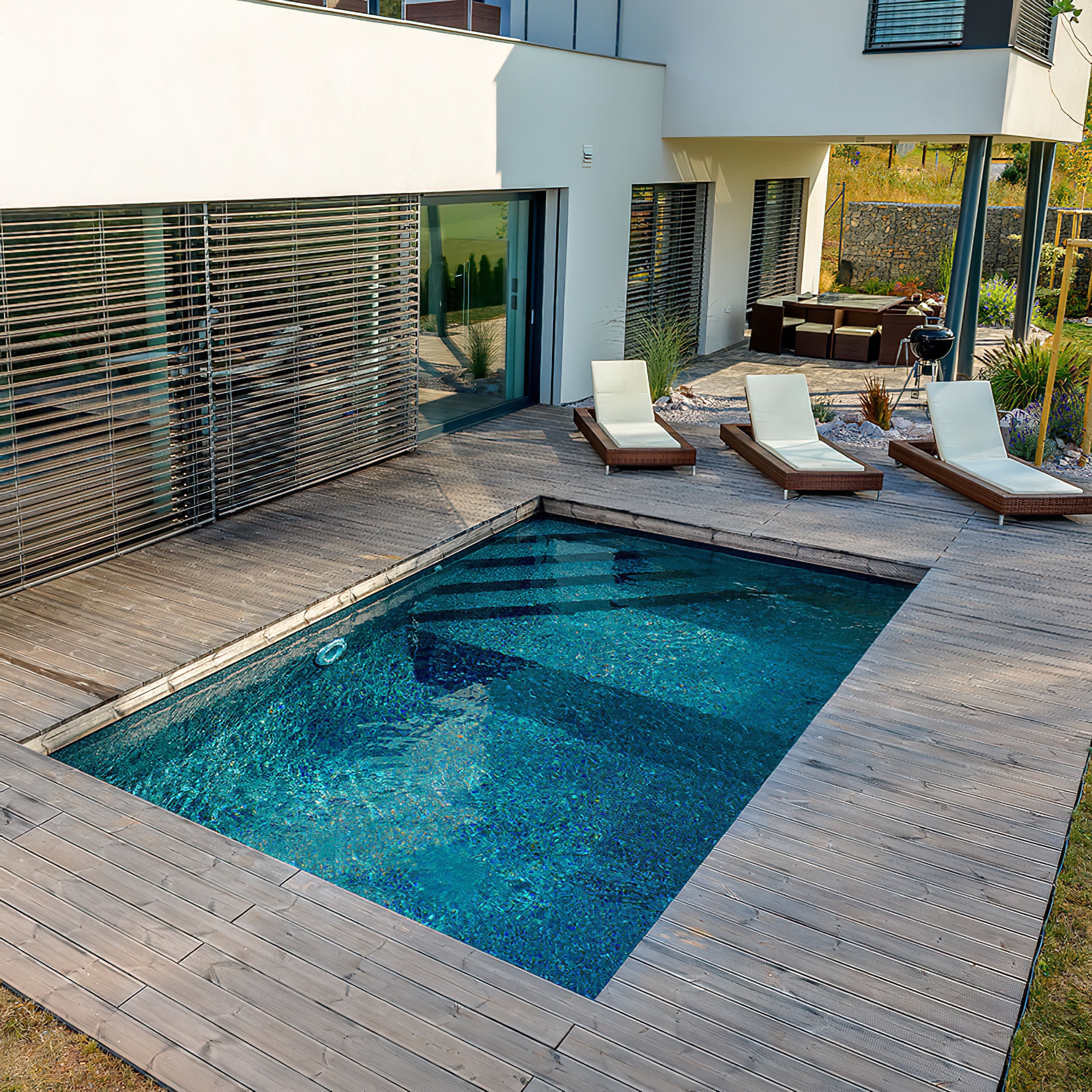 Piscina rettangolare in giardino con terrazza in legno e lettini bianchi